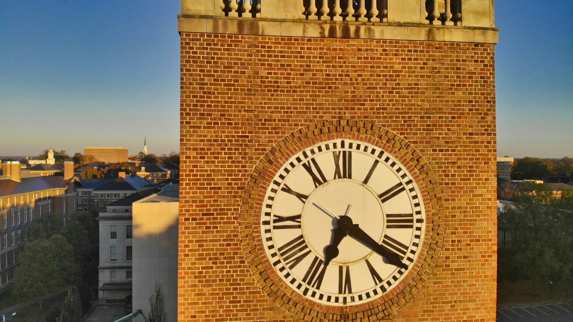 Close-up of a brick clock tower with Roman numerals showing 4:20 against a clear blue sky.