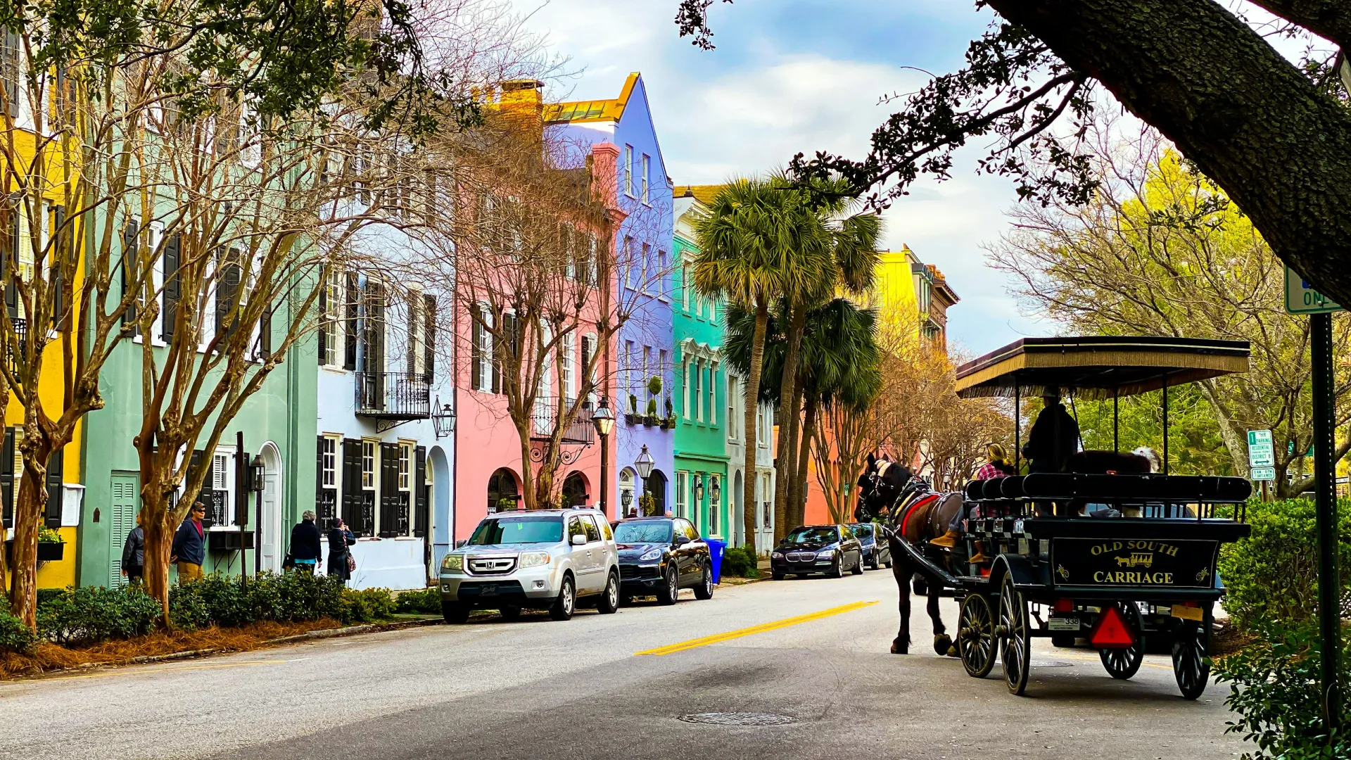 Colorful historic buildings line a street with parked cars and a horse-drawn carriage under bare trees.