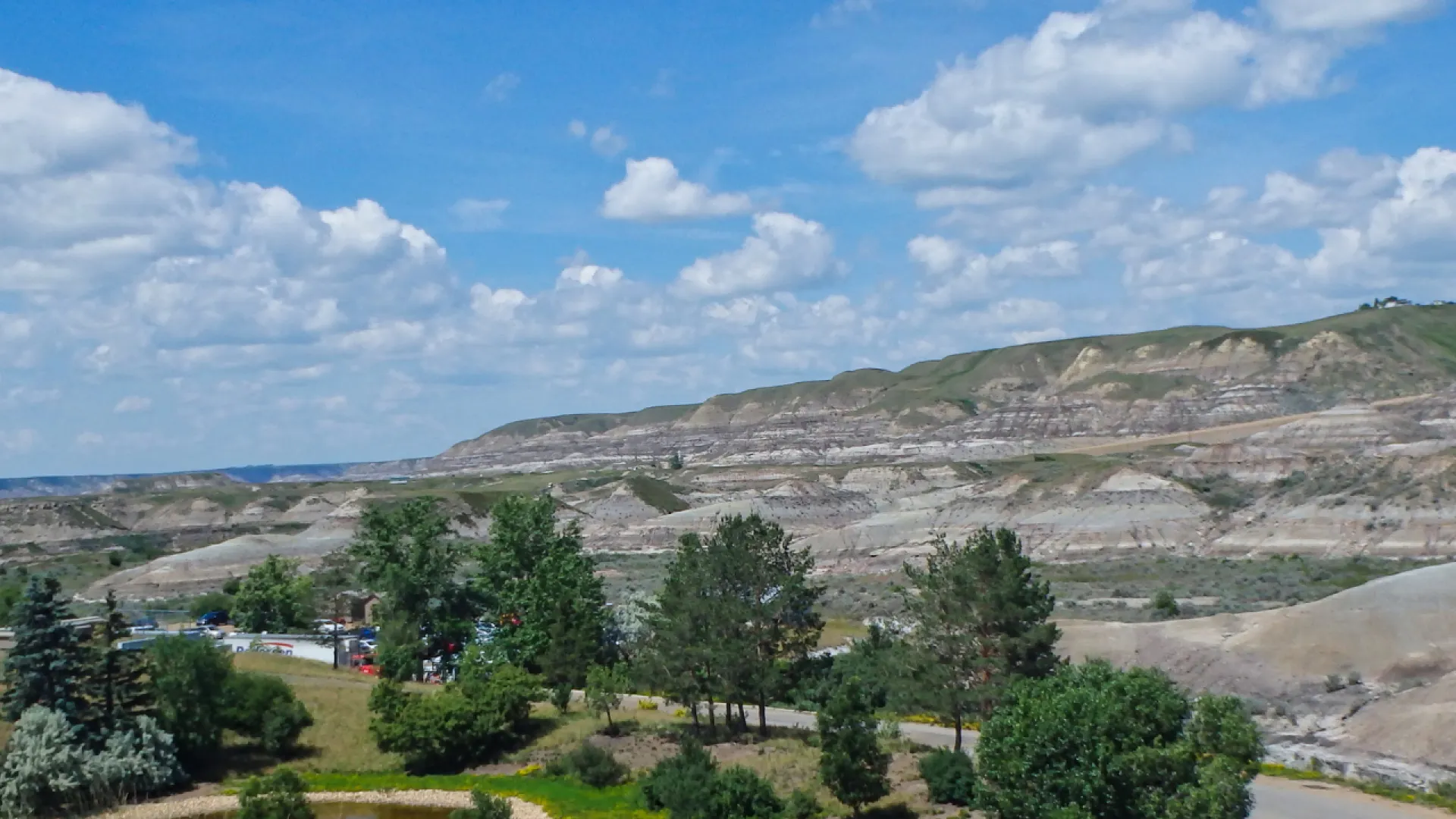 Expansive view of a rocky desert landscape with green trees under a blue sky with scattered white clouds