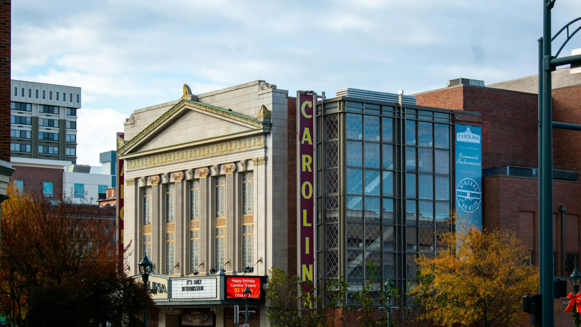 Historic Carolina Theatre building with ornate columns and colorful marquee in an urban setting with fall trees.