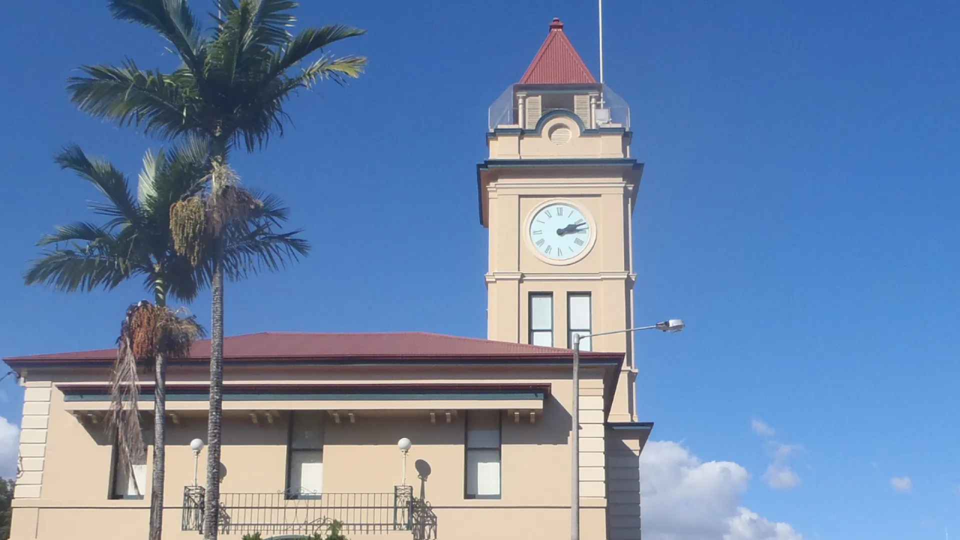 Historic clock tower with red roof and palm trees under a clear blue sky.