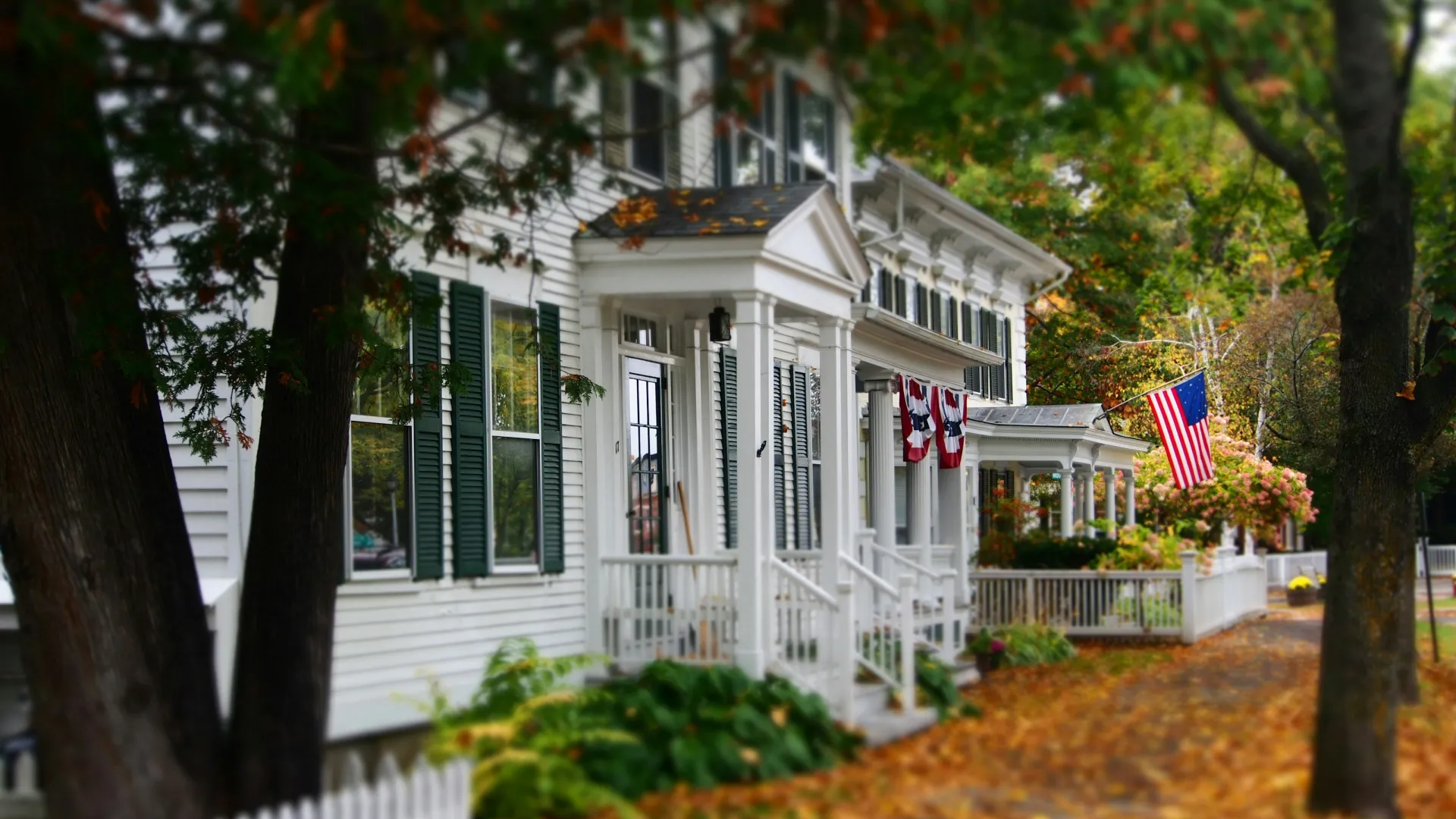 a white house with green shutters and a flag on the porch