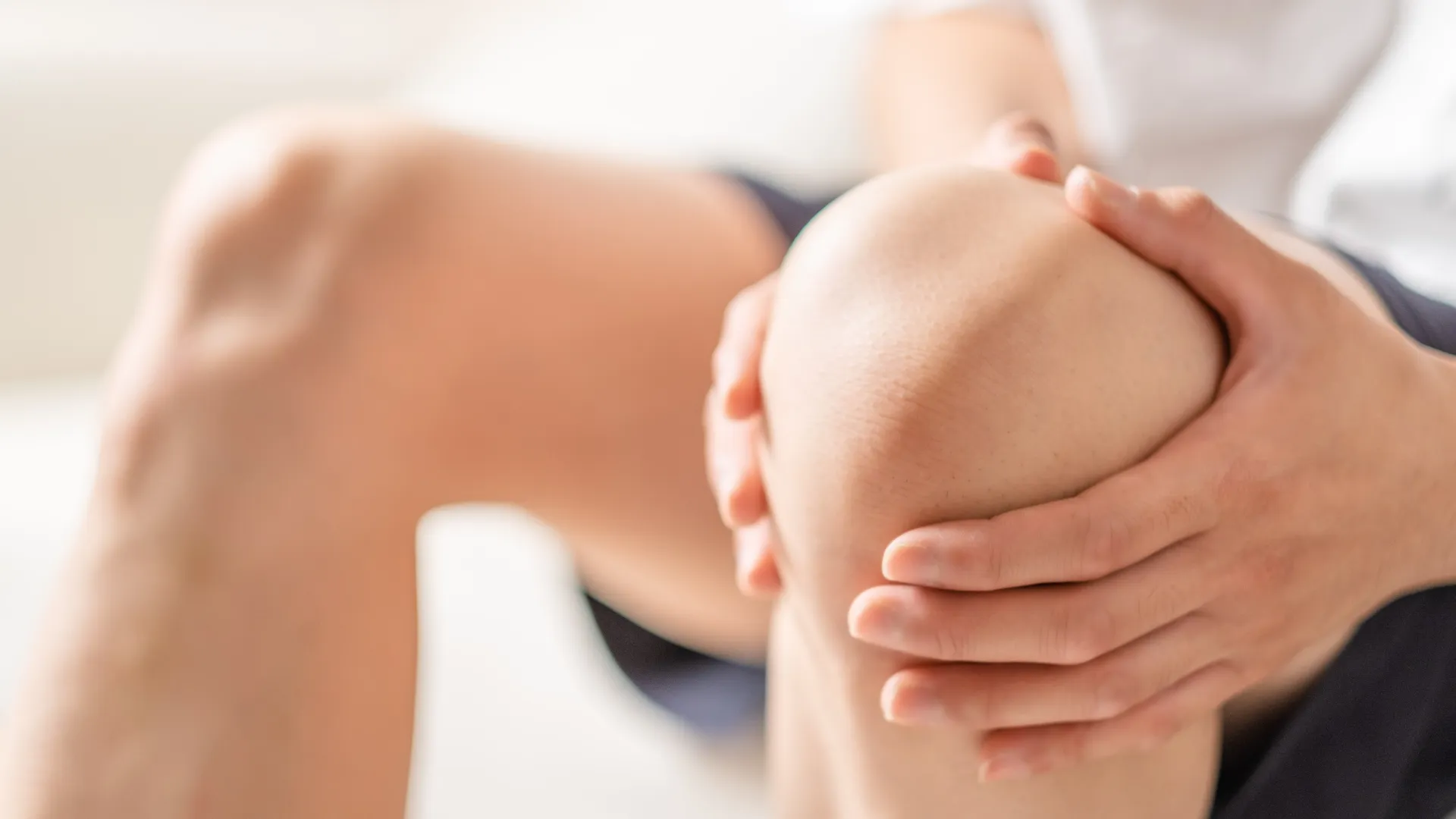 Person holding their knee in pain, showing discomfort and possible injury or joint pain indoors.