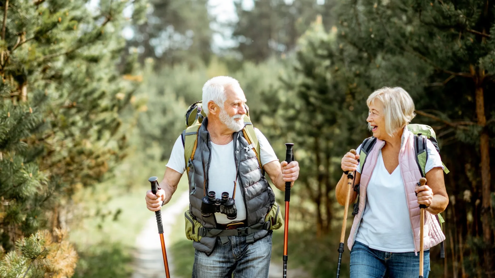 Senior couple hiking with backpacks and walking sticks on a forest path enjoying nature outdoors