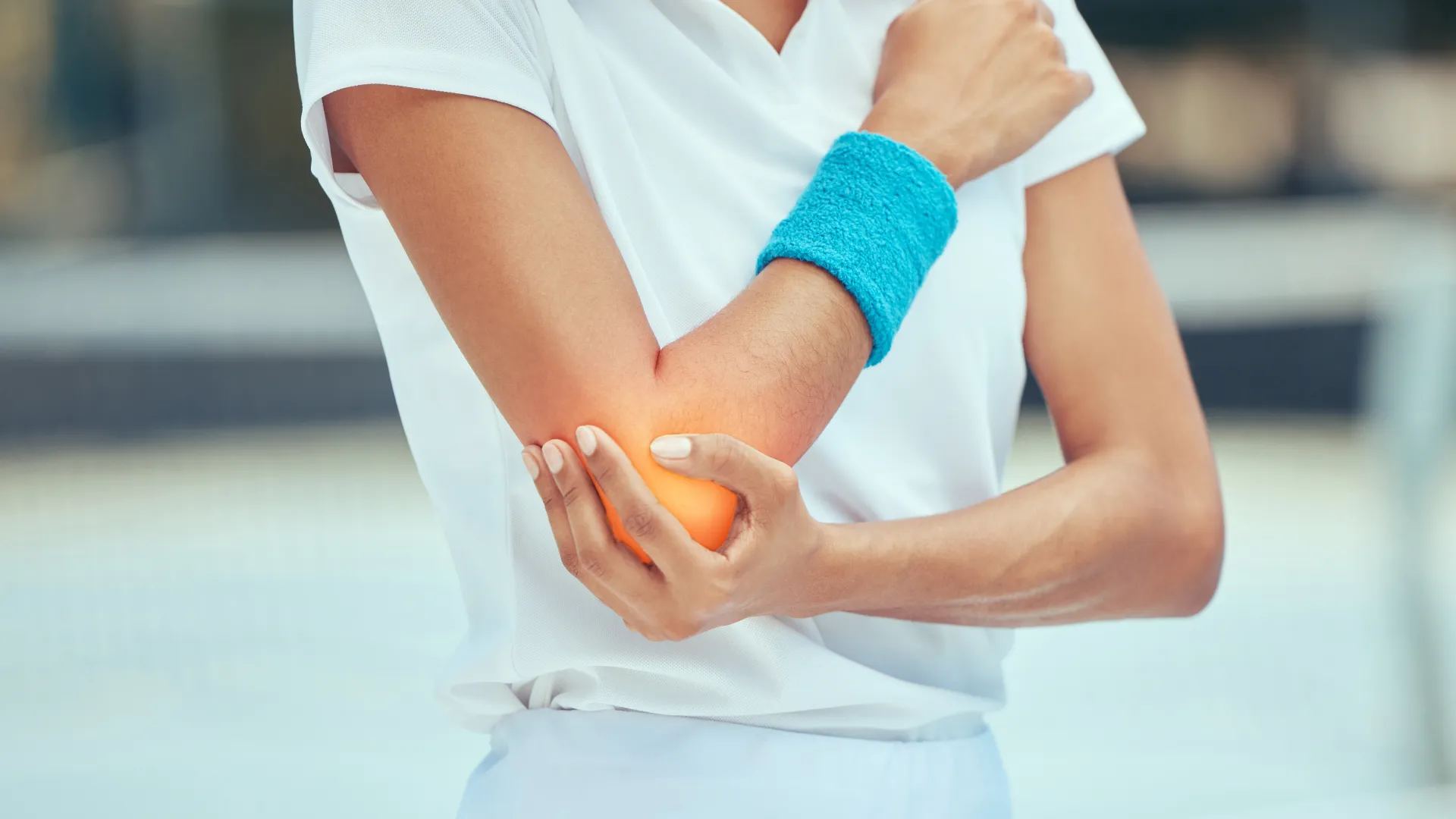 Person in white sportswear holding painful elbow with a blue sweatband, indicating elbow pain or injury.