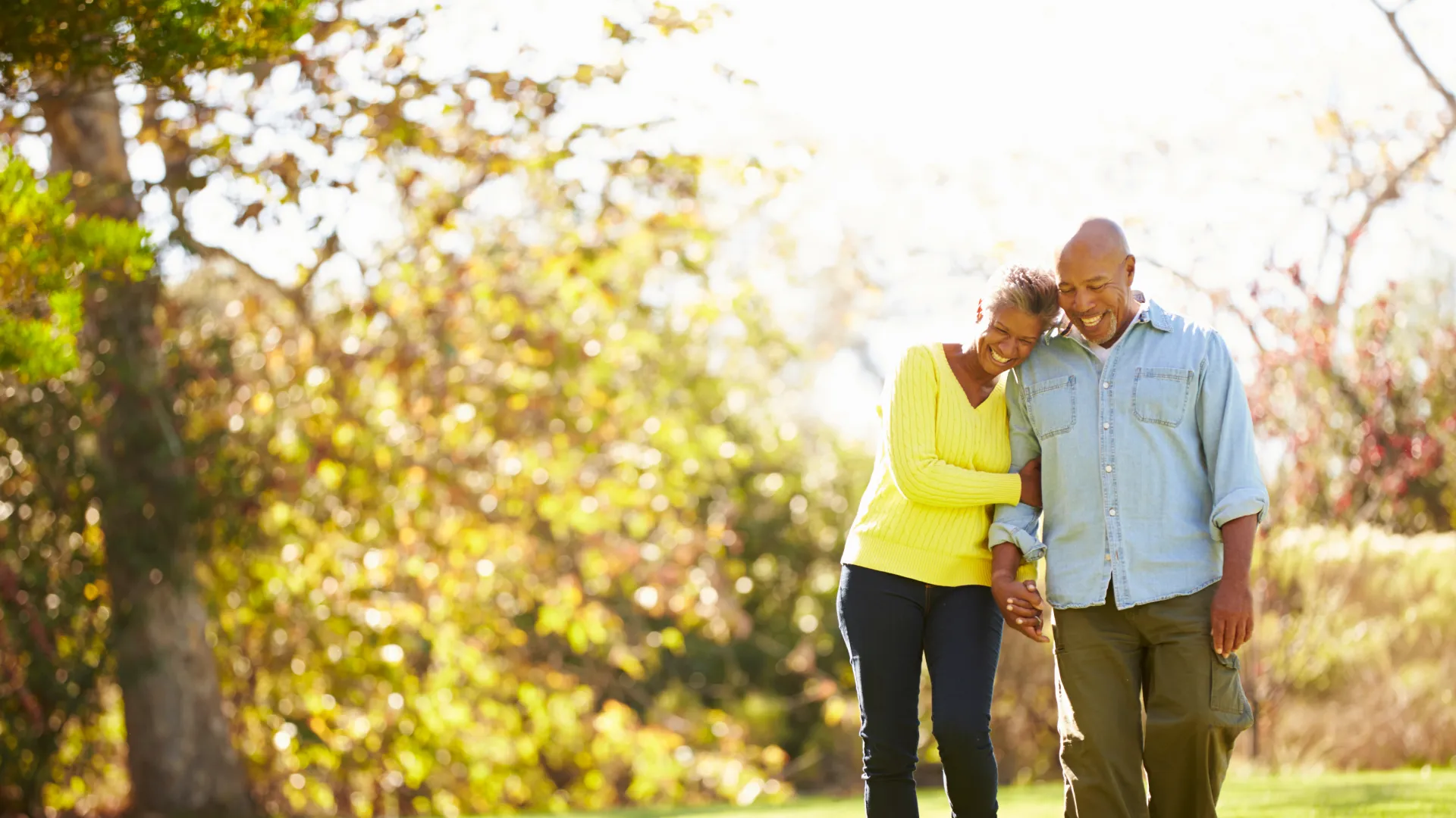 Couple walking outdoors in autumn holding hands and smiling with trees and grass in the background
