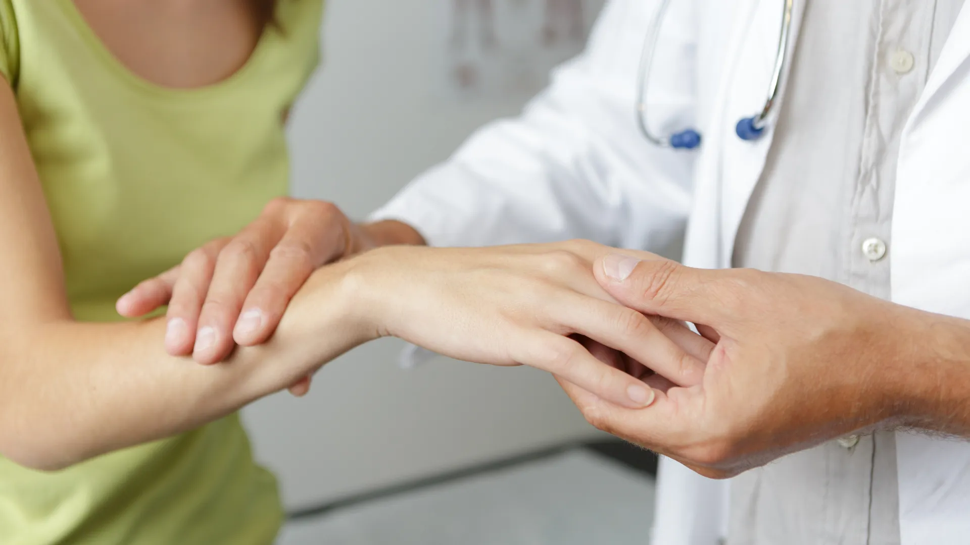 Doctor examining a female patient's wrist and hand in a medical office setting with gentle care.