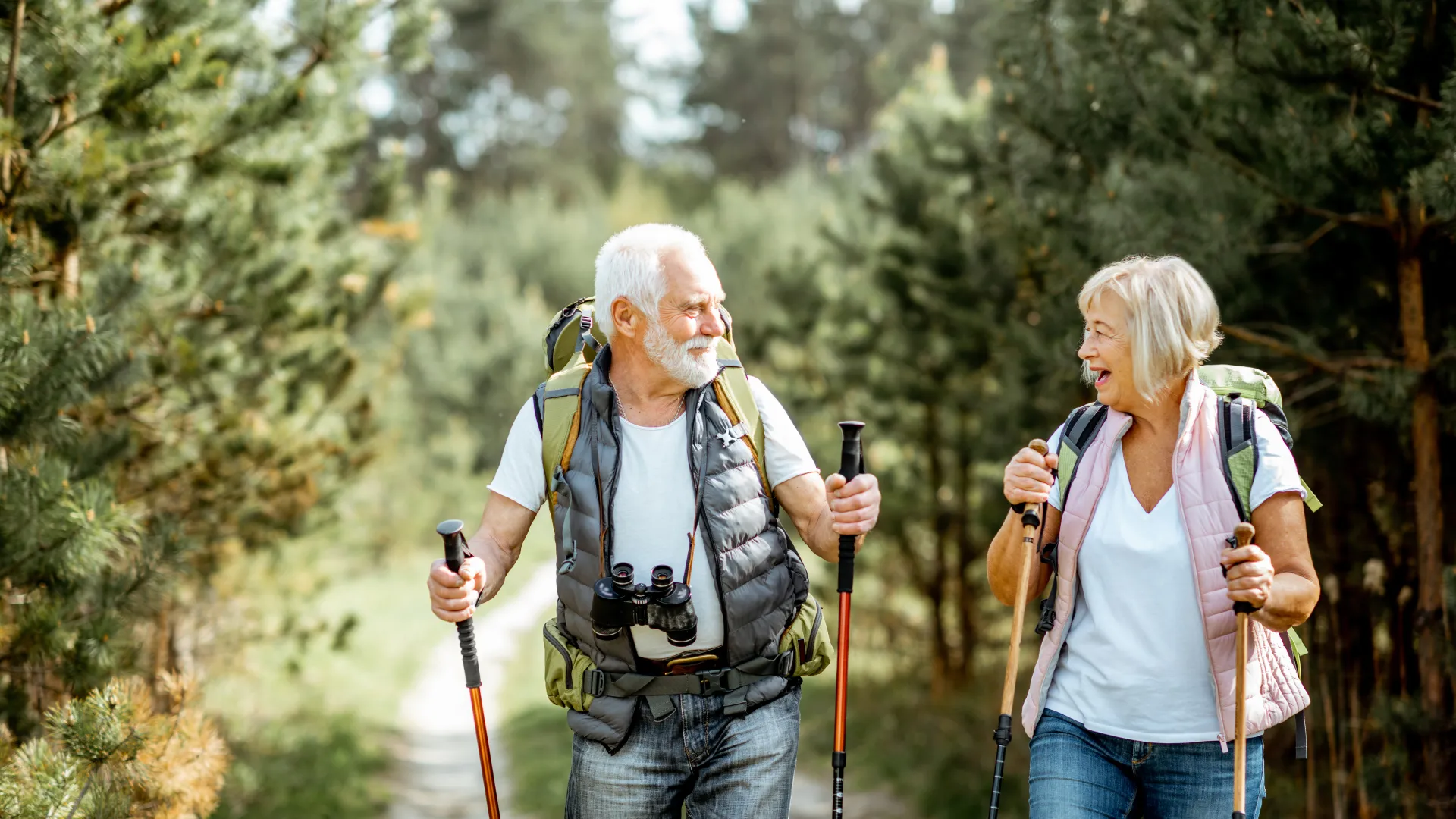 Senior couple hiking with backpacks and walking poles on a forest trail, enjoying nature and each other's company.
