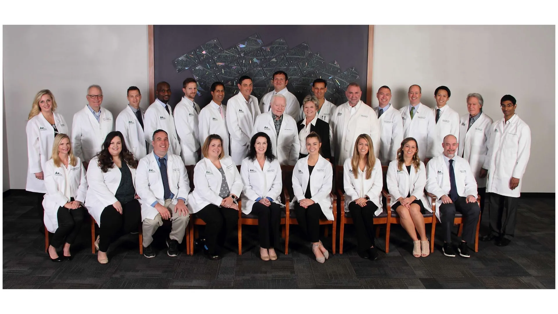 Group of diverse medical professionals wearing white lab coats posing for a formal team photo indoors.