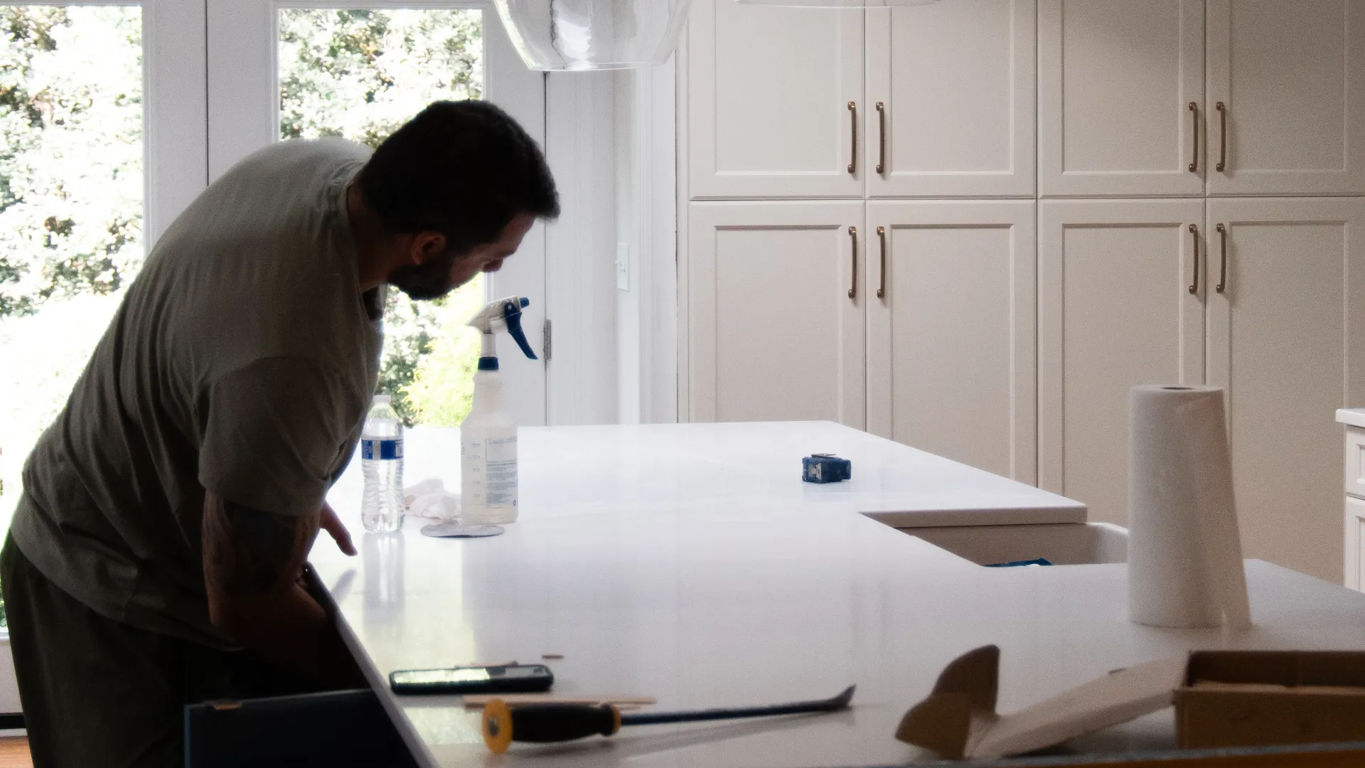 Man working on kitchen island renovation under pendant lights in modern white kitchen with cabinets.