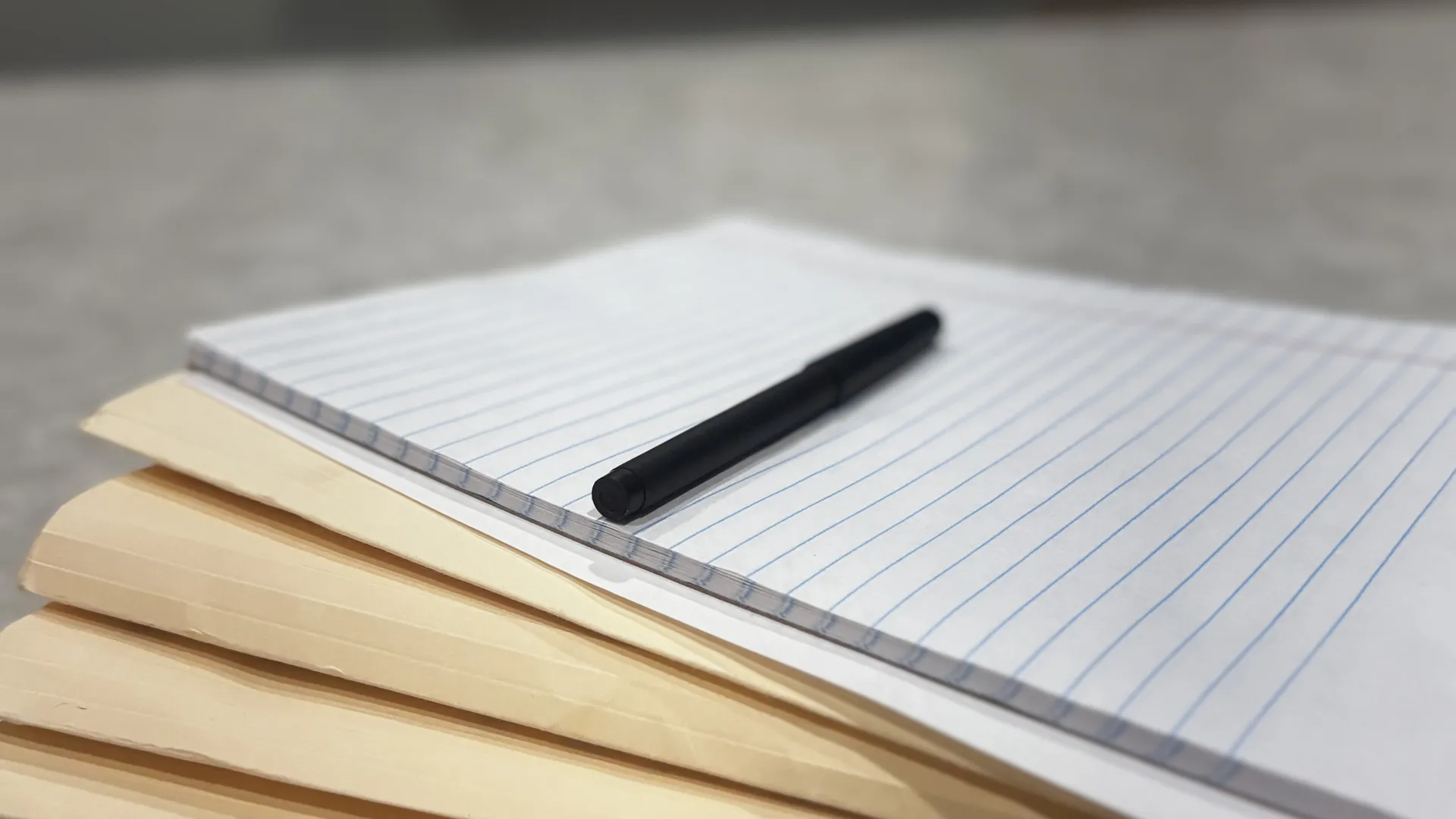 Stack of yellow folders with a lined notepad and black pen on a gray marble surface.