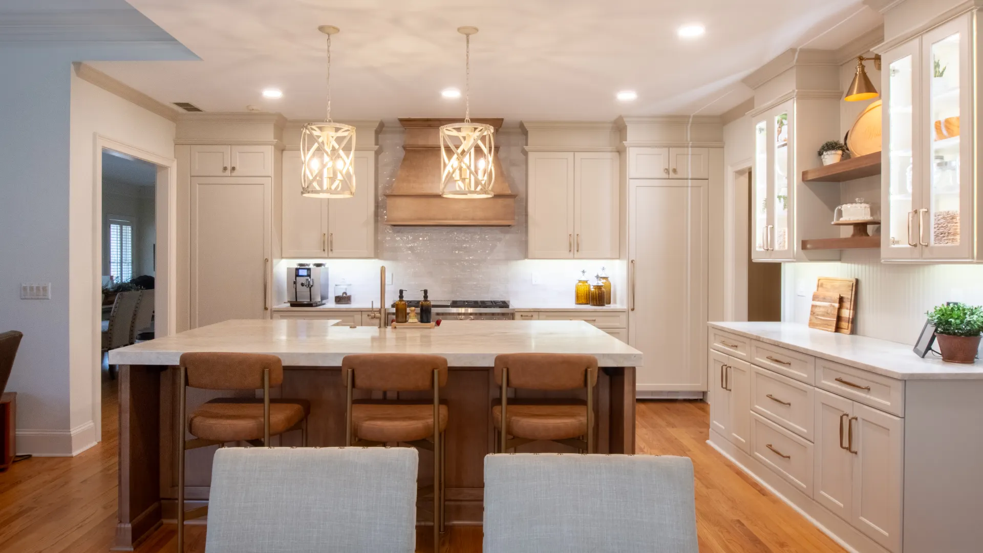 Modern kitchen with white cabinets, wooden island, pendant lights, and hardwood floors under warm lighting.