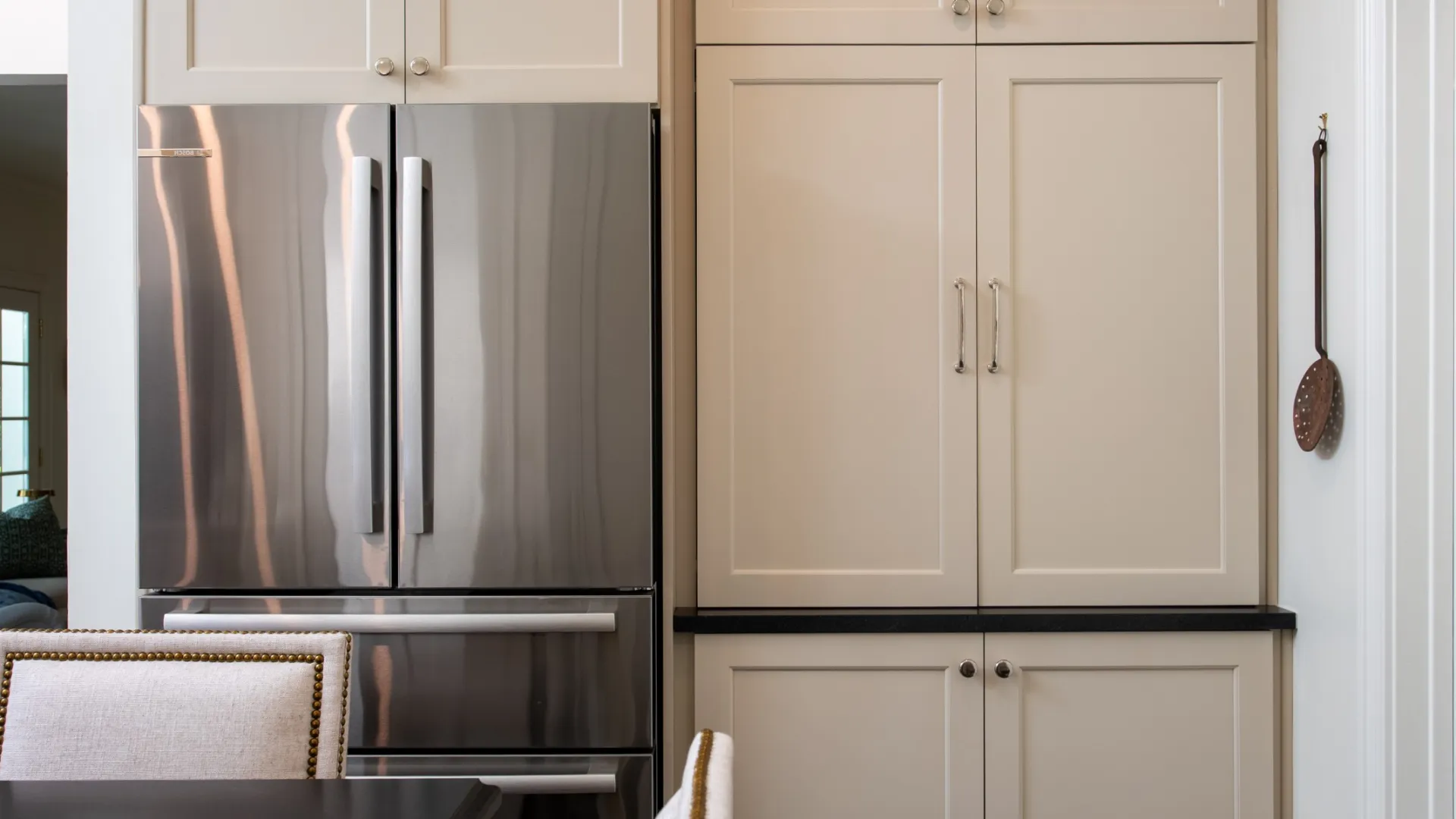 Modern kitchen with beige cabinets, stainless steel refrigerator, and dining table with upholstered chairs.