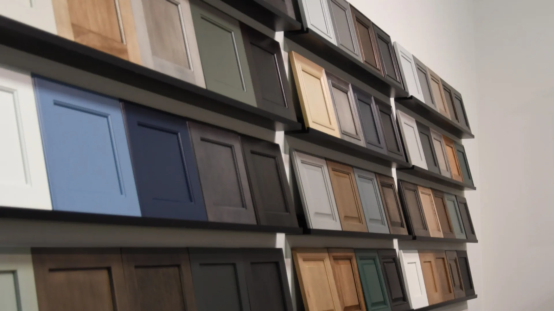 Wall display of various kitchen cabinet door samples in multiple colors and finishes for home remodeling.