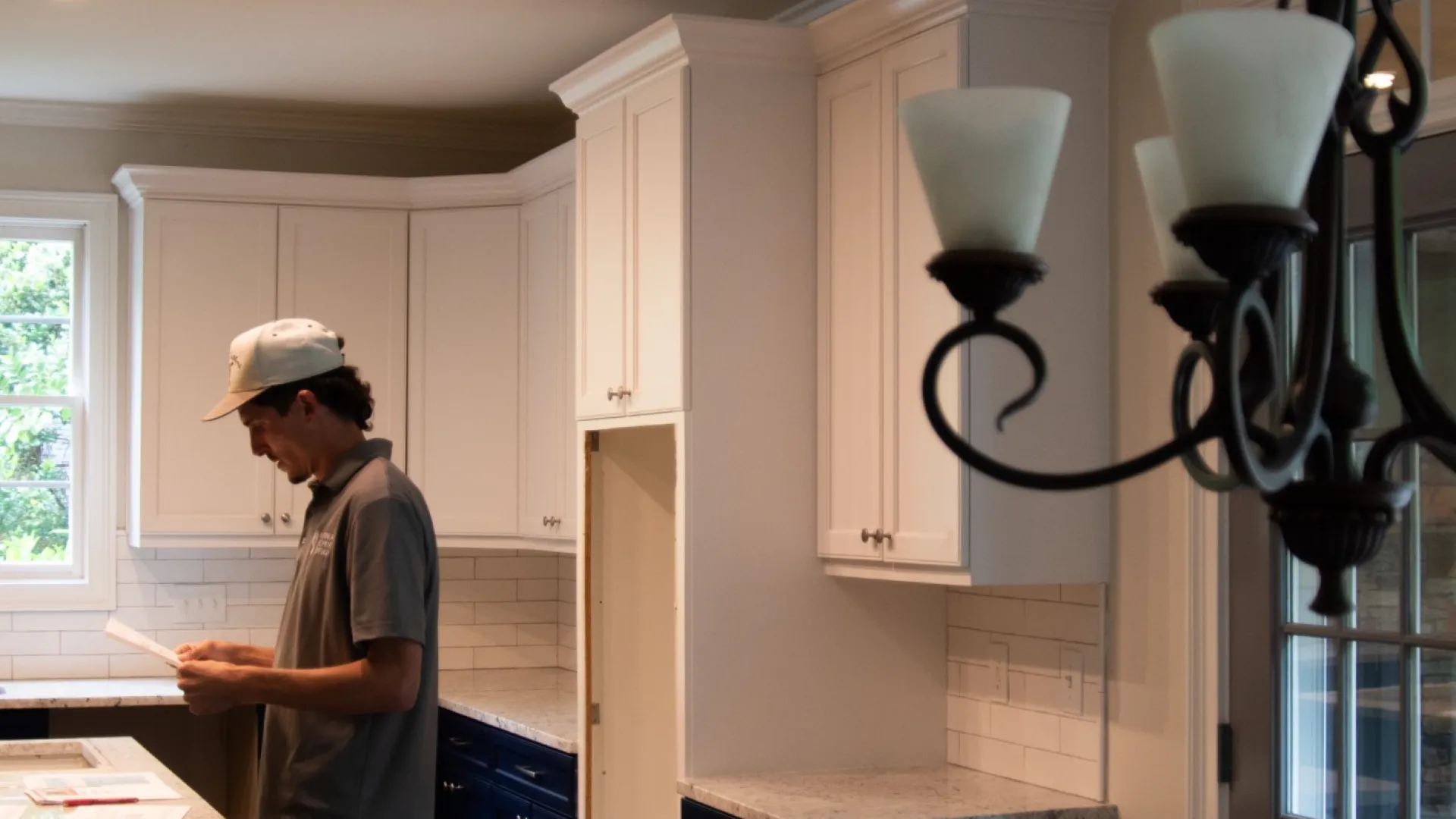 Man reviewing documents in a modern kitchen with white upper cabinets and dark blue lower cabinets.