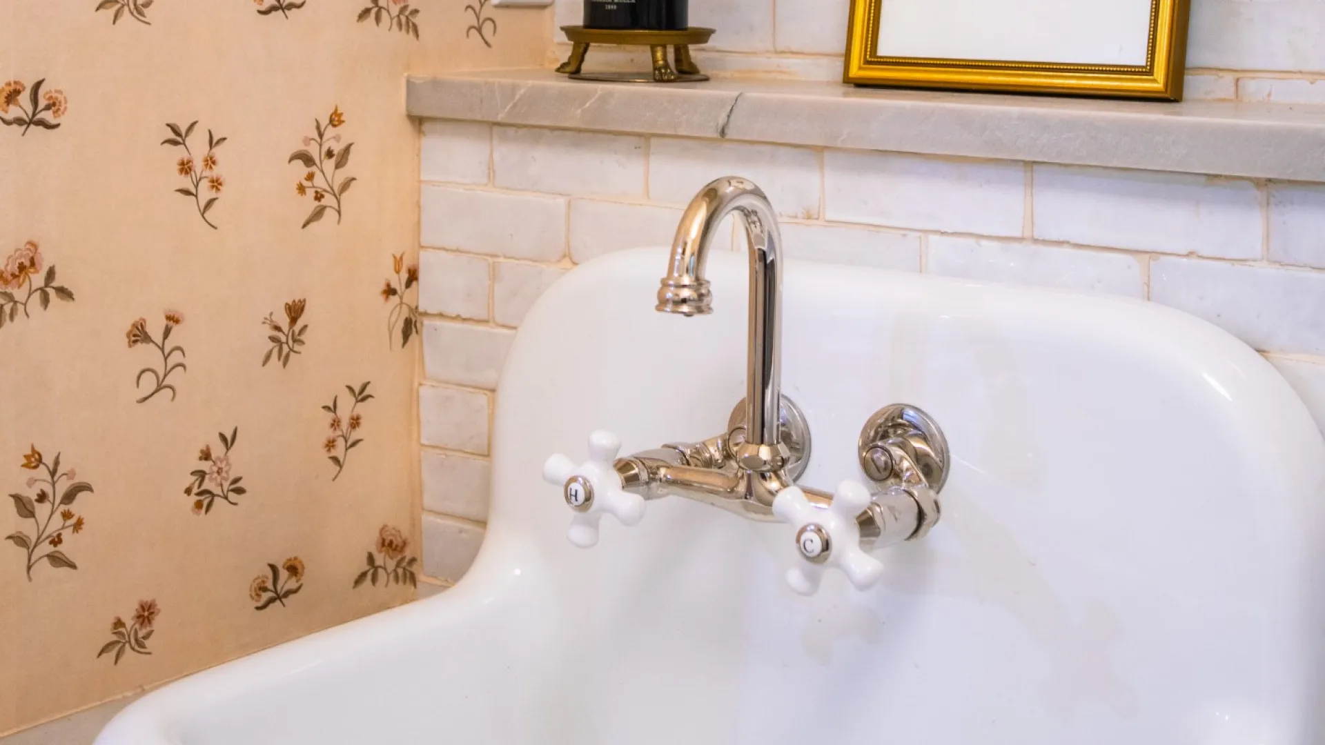 Vintage white porcelain sink with chrome faucet, floral wallpaper, and framed dog picture in a cozy bathroom.