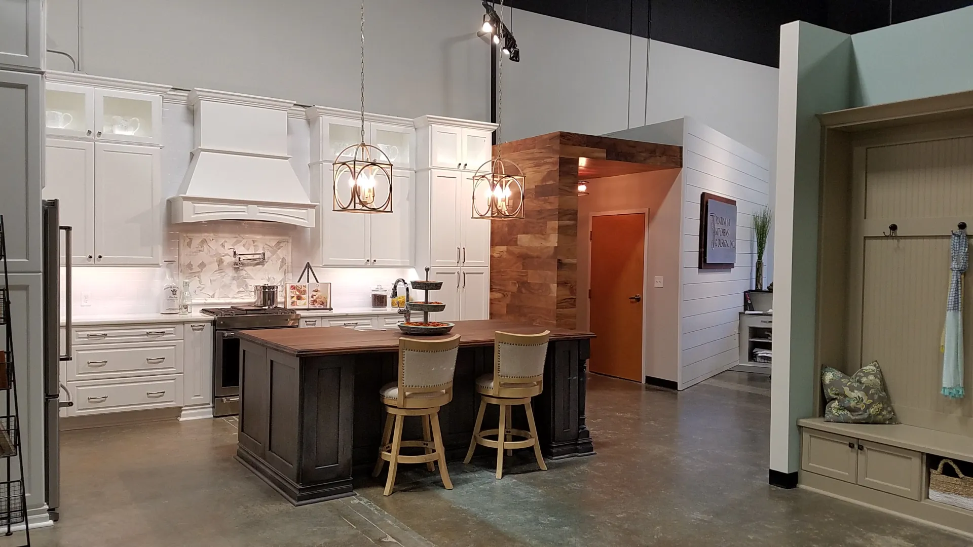 Modern kitchen with white cabinetry, a dark wood island, two chairs, pendant lighting, and concrete flooring.