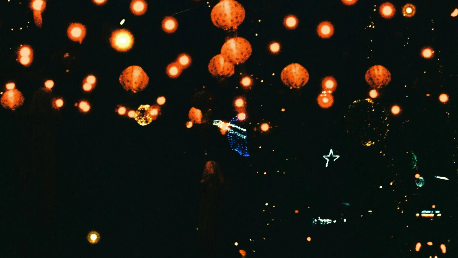 Warm glowing orange lanterns and lights hanging in a dark nighttime setting creating a festive atmosphere.