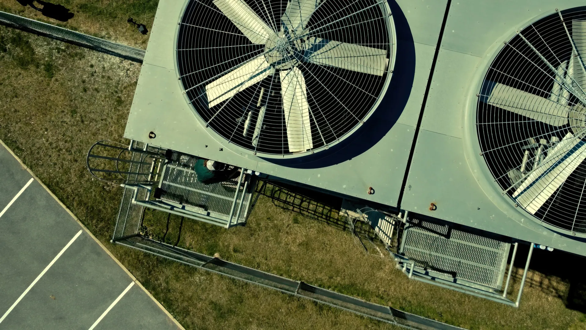 Aerial view of large industrial cooling fans installed on equipment outside near parking and grassy area.
