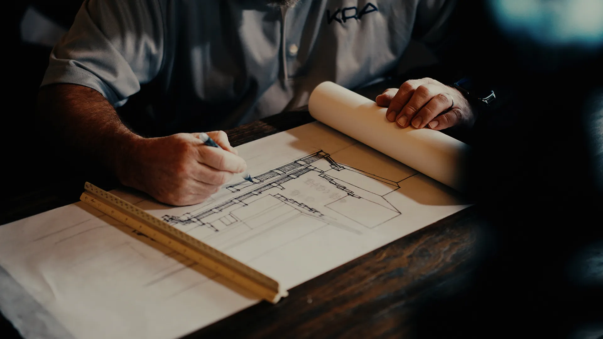 Architect working on building blueprint with ruler on wooden table in dim light.