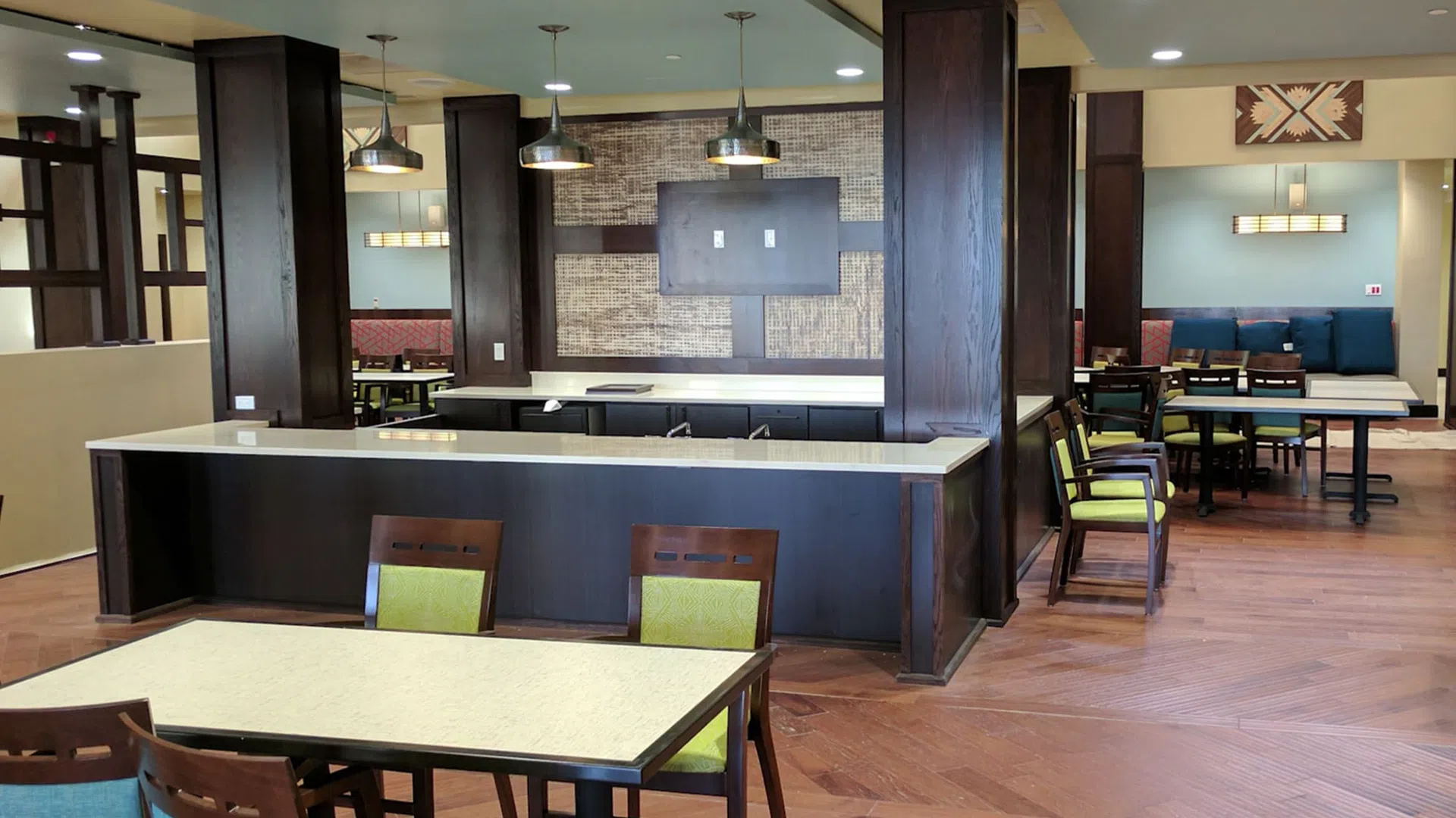 Modern dining area with wooden tables and chairs featuring green cushions and pendant lighting in a spacious room.