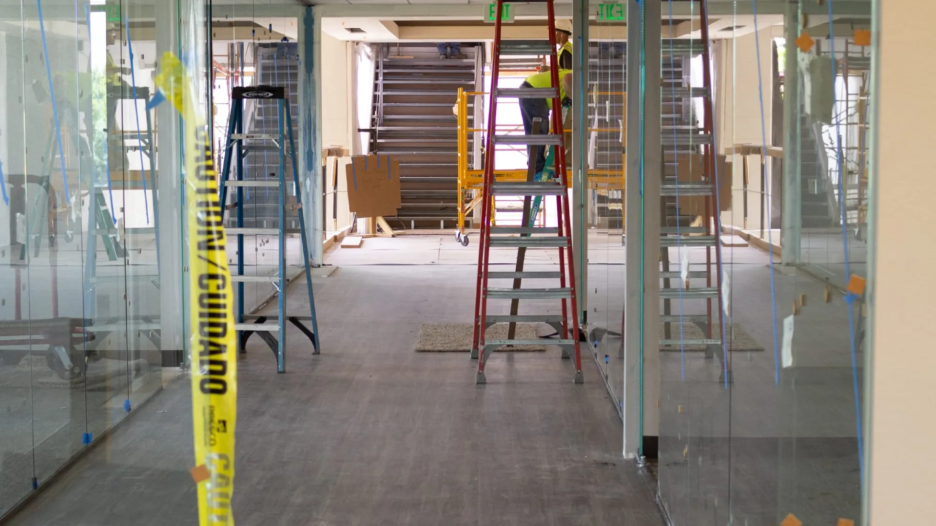 Interior office under construction with ladders, glass walls, and caution tape in a modern building space.
