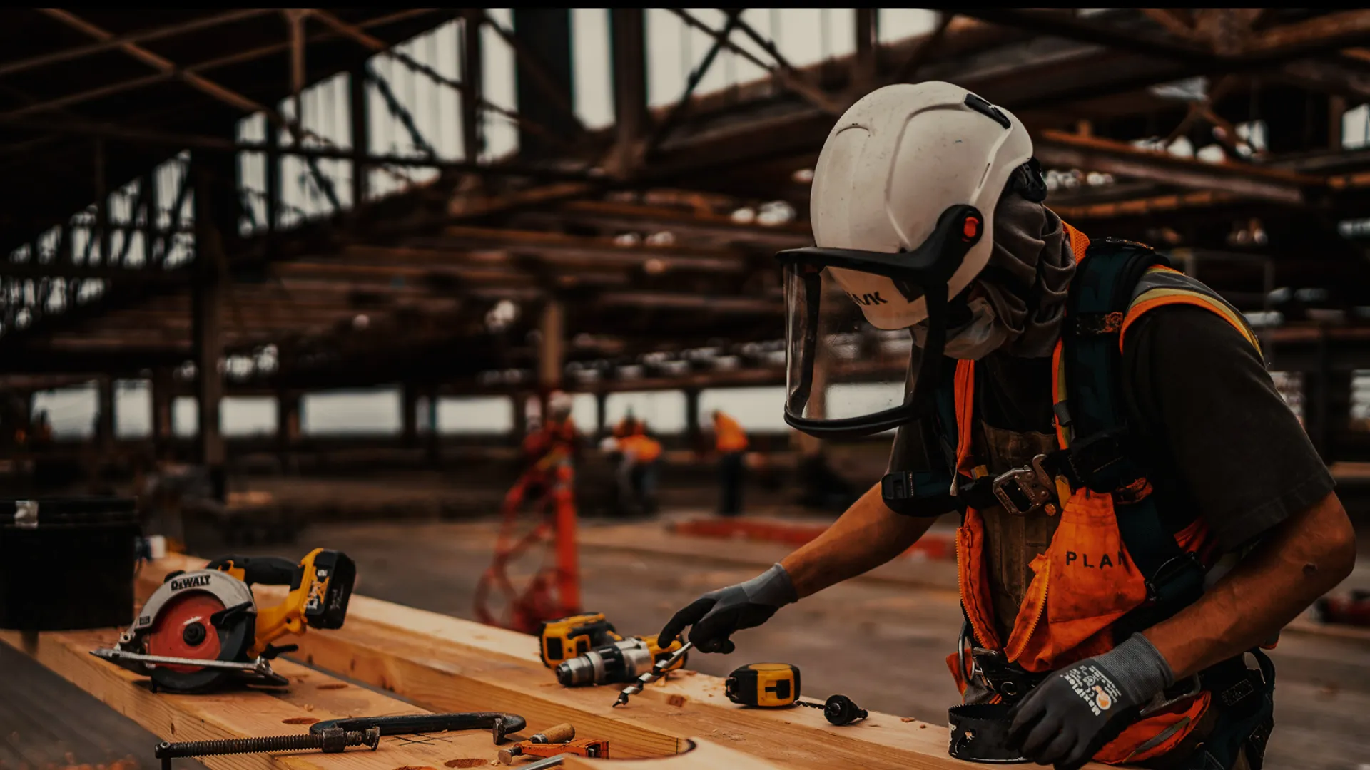 Construction worker wearing safety gear assembling wooden beams inside an industrial building under construction.