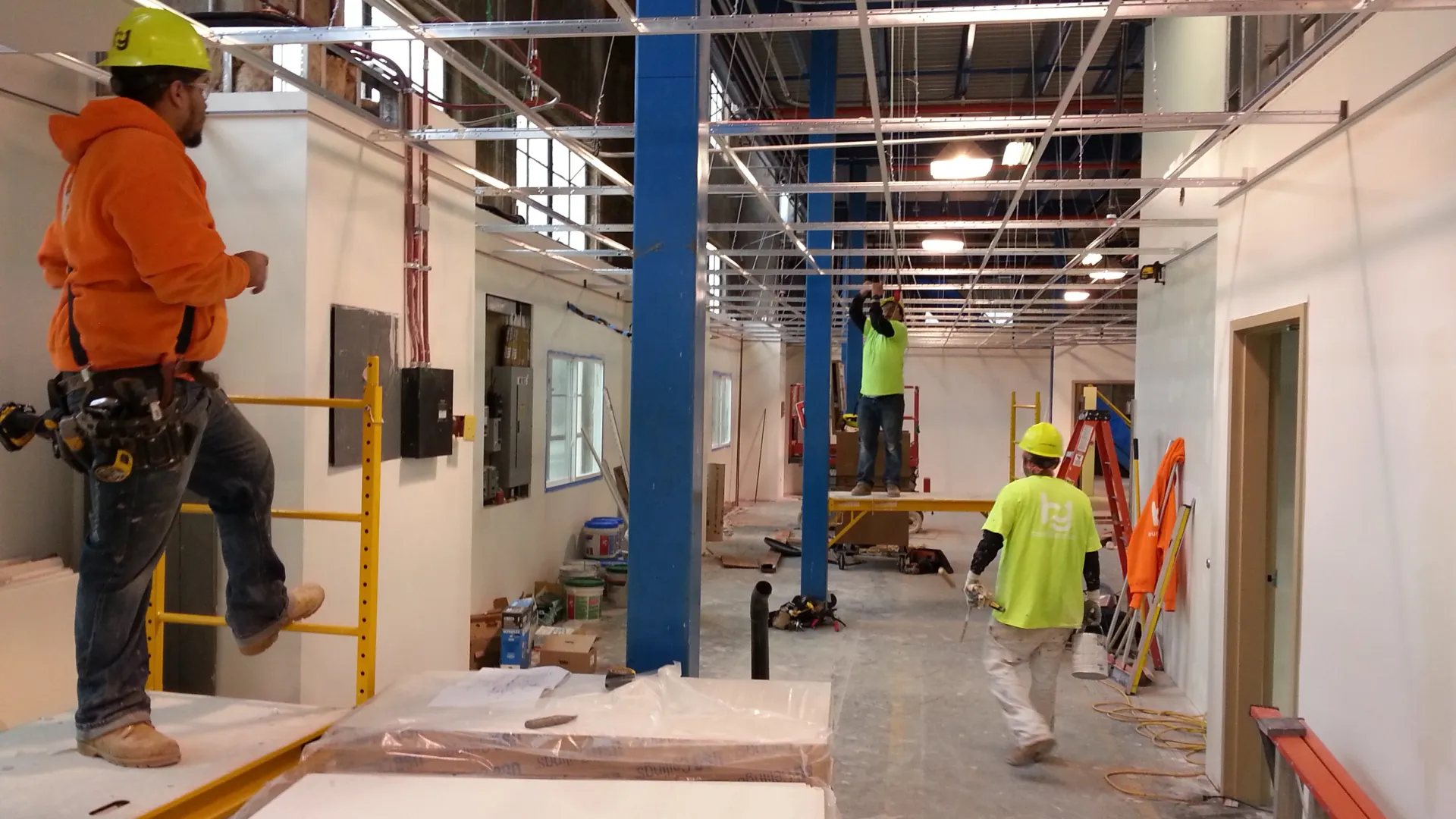 Construction workers installing ceiling framework in a commercial building under renovation.