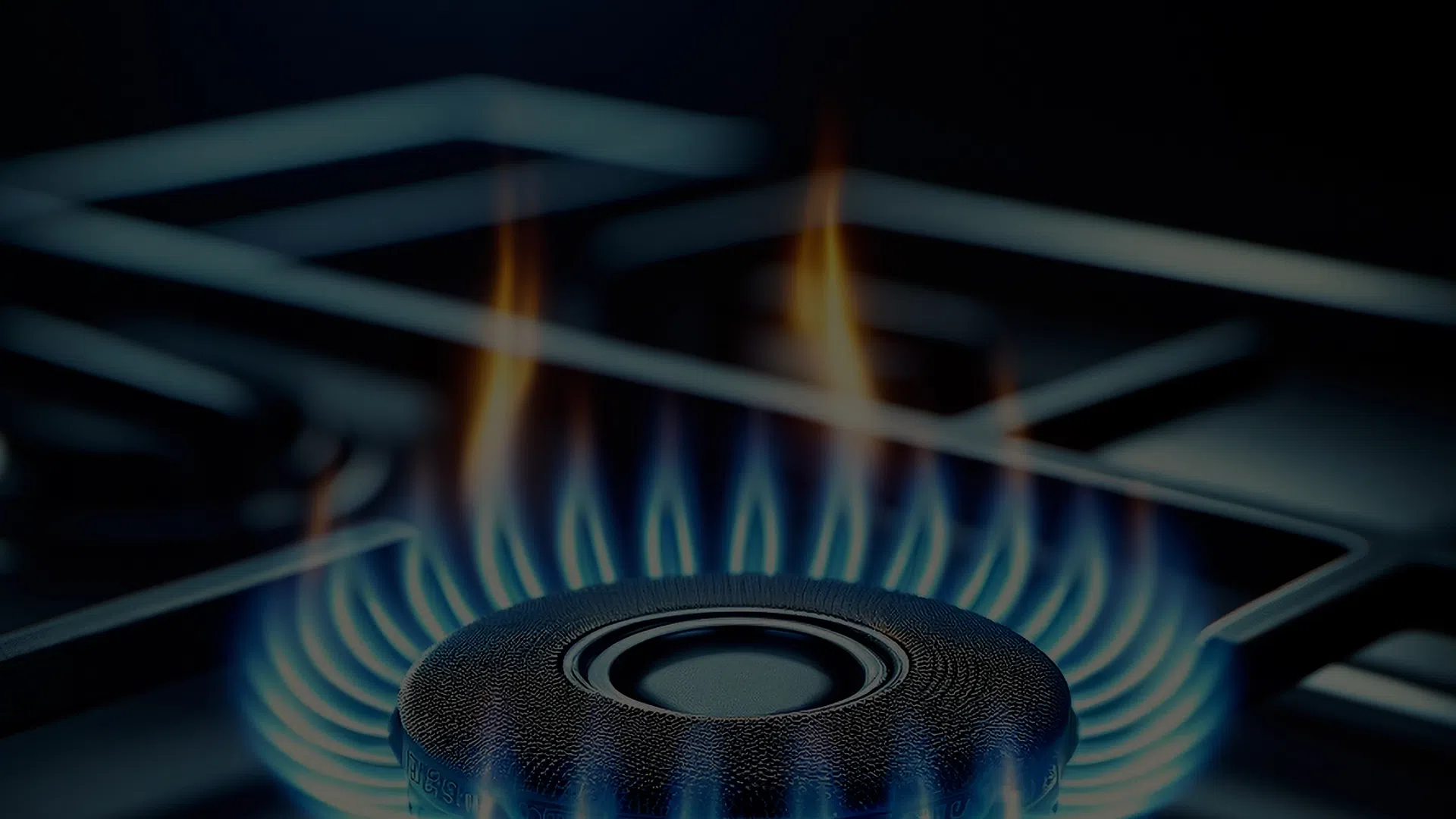 Close-up of a blue gas flame burning evenly on a stove burner in a dark kitchen setting.