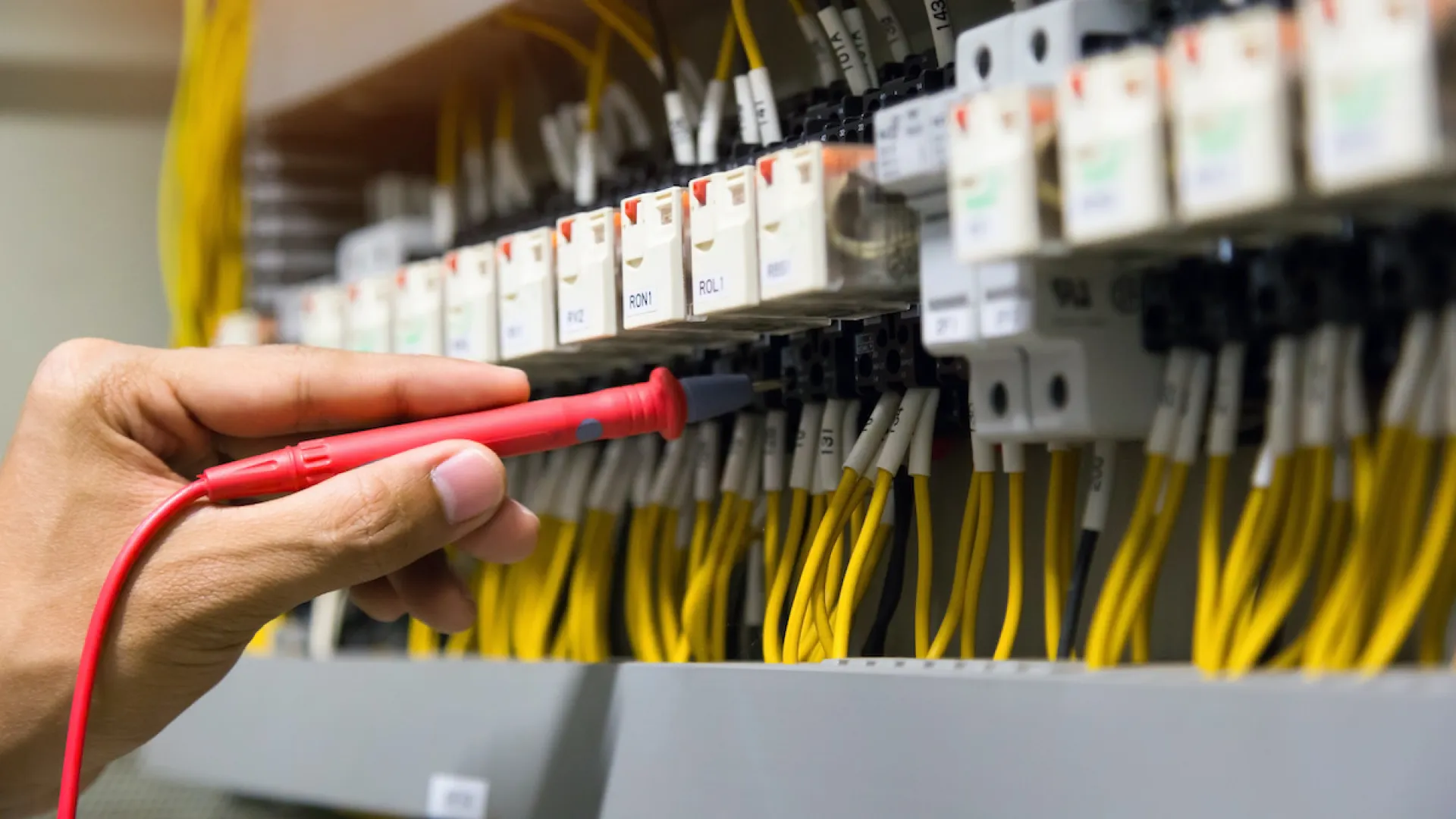 Close-up of a hand using a multimeter on electrical circuit breakers and wiring.