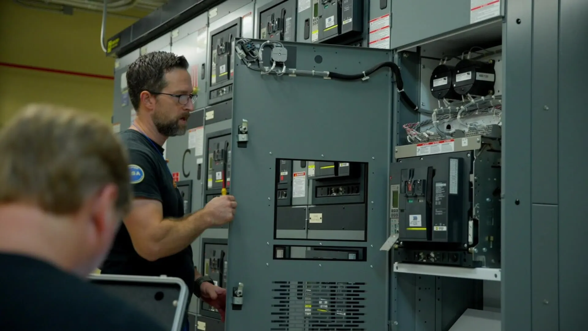 Technician inspecting and working on an industrial electrical control panel with circuit breakers and wiring.