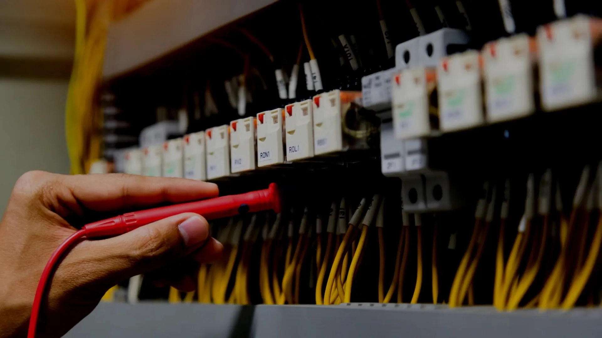 Technician testing electrical connections with a red probe on a circuit breaker panel with yellow wires