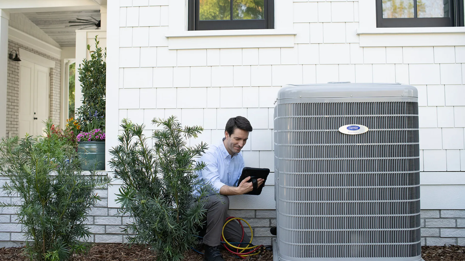 Technician checking air conditioning unit settings with a tablet outside a modern home.