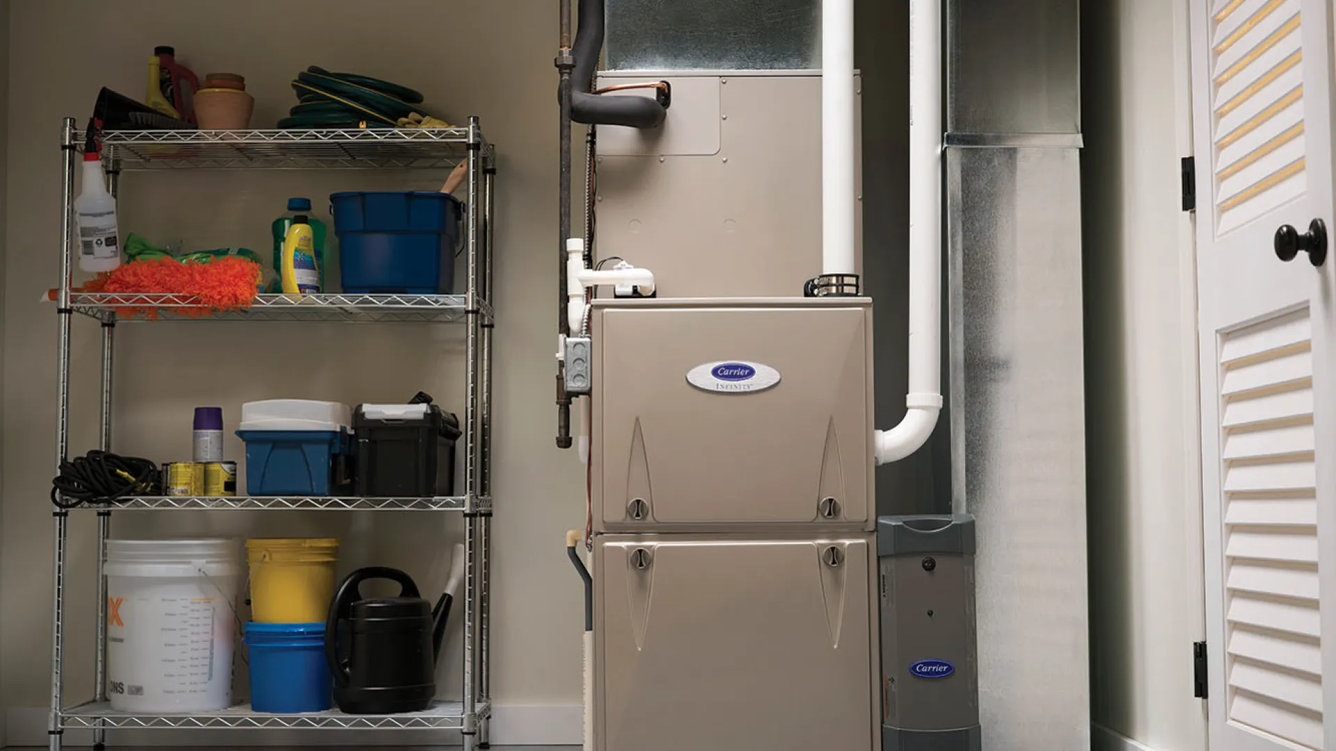 Utility room with a Carrier furnace unit beside metal shelving holding cleaning and gardening supplies