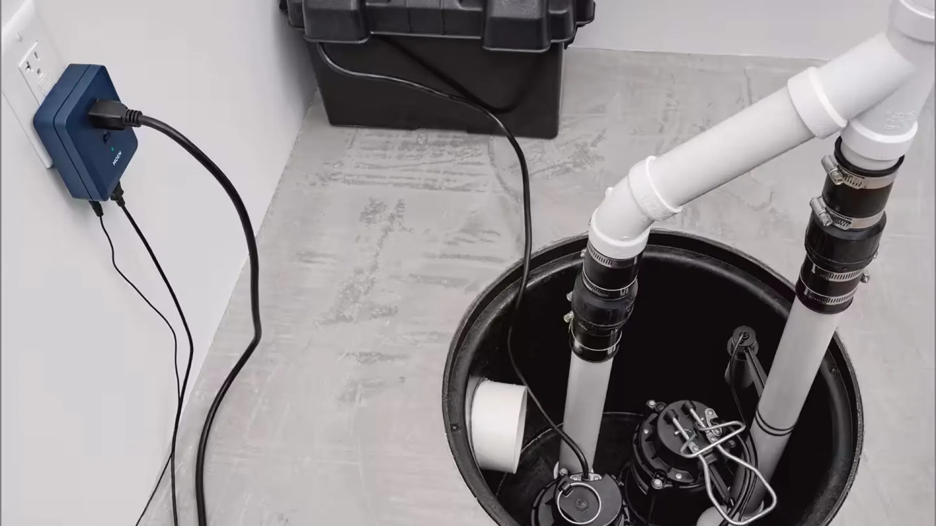 Sump pump system installed in basement with connected pipes and electrical cords plugged into wall outlet.