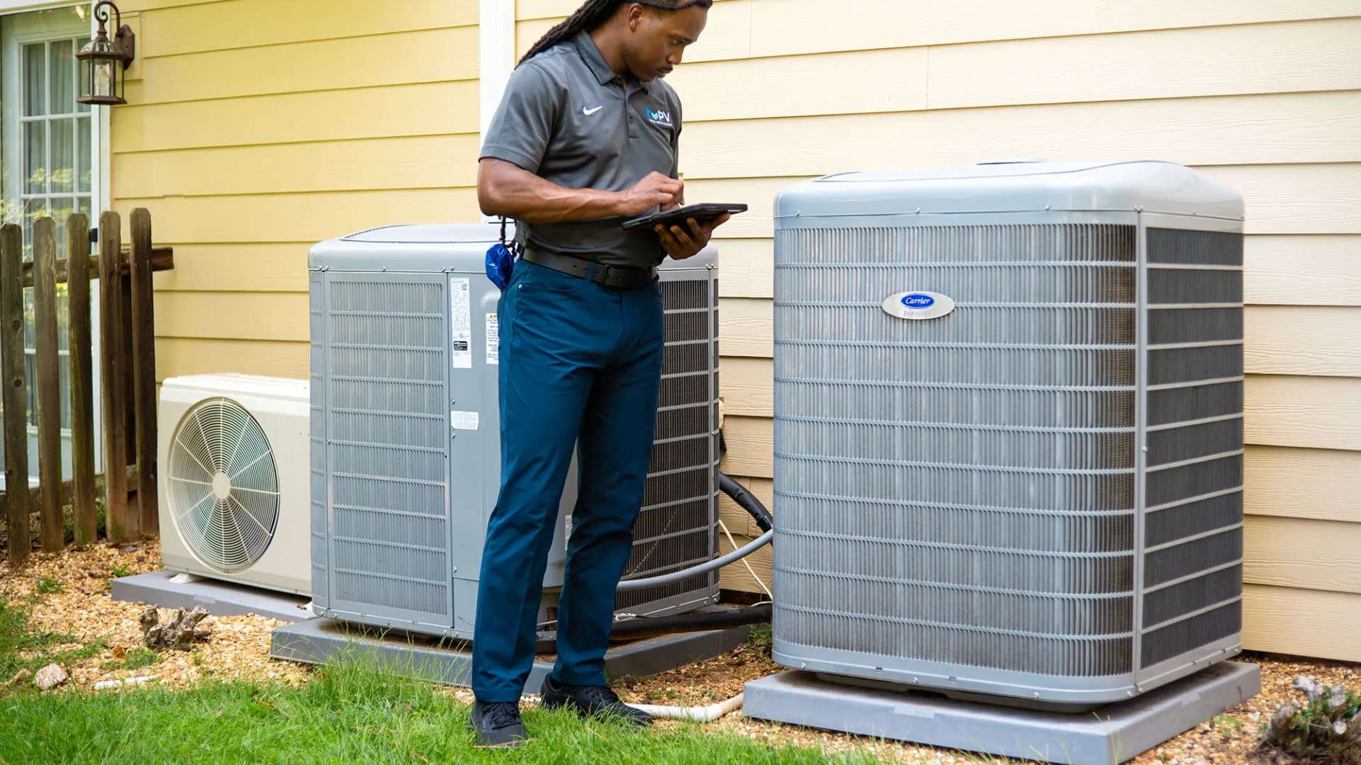 Technician inspecting and documenting the condition of three outdoor air conditioning units beside a house.