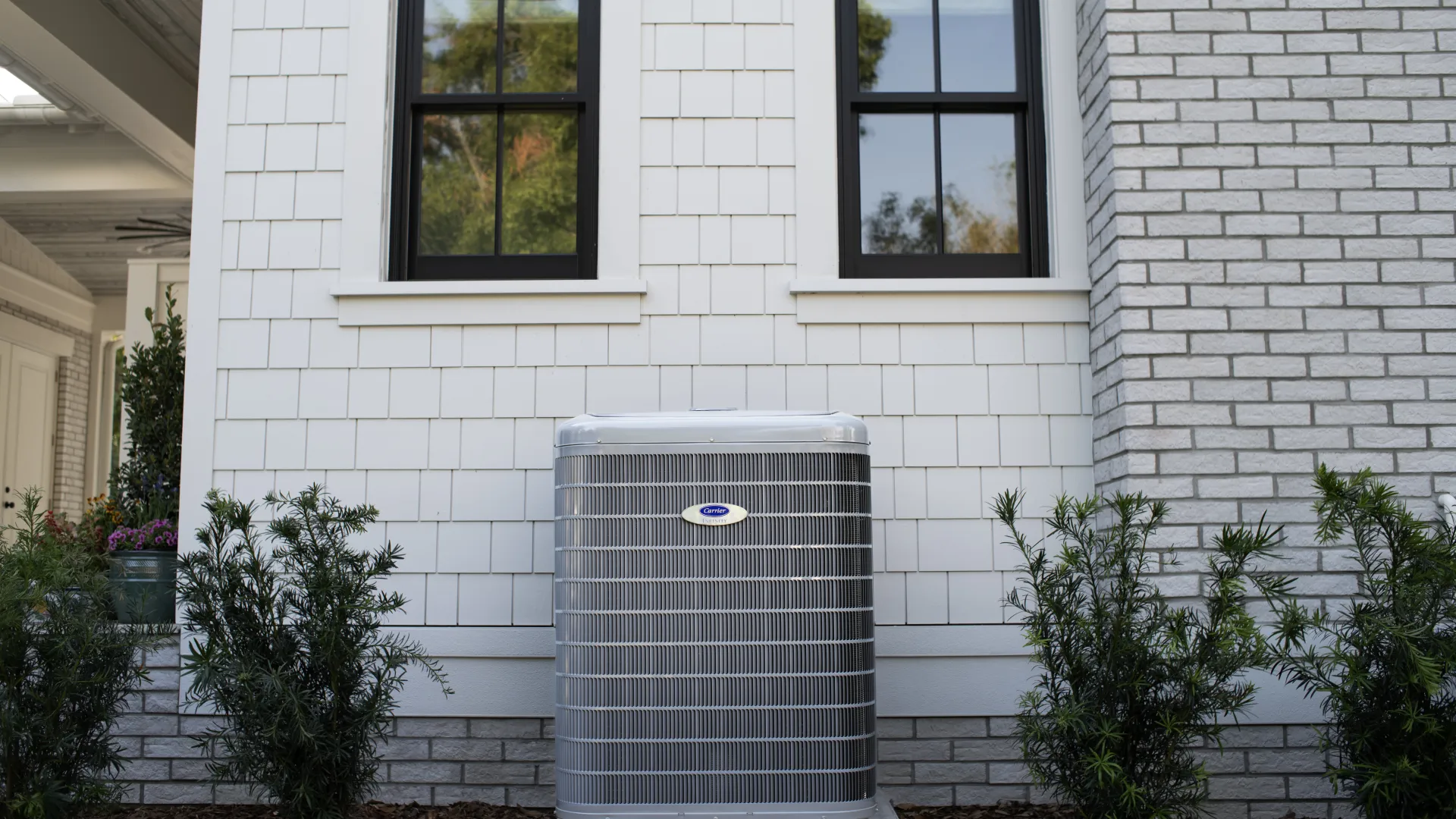 Cool and modern outdoor air conditioning unit next to a stylish, white shingle house.