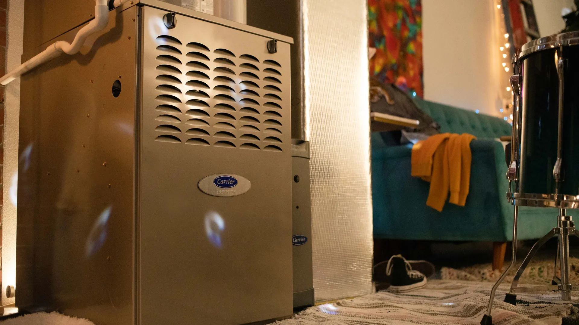 Carrier furnace unit installed in a cozy living room with a teal couch and musical instruments nearby