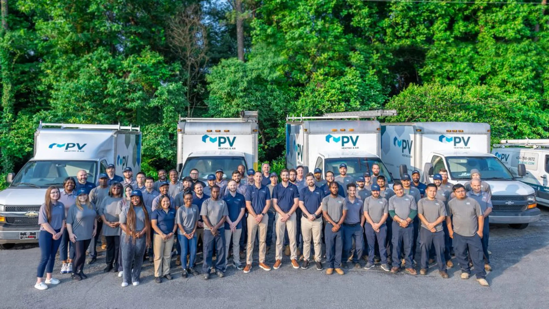 A team of professionals posing in front of company trucks surrounded by lush greenery.