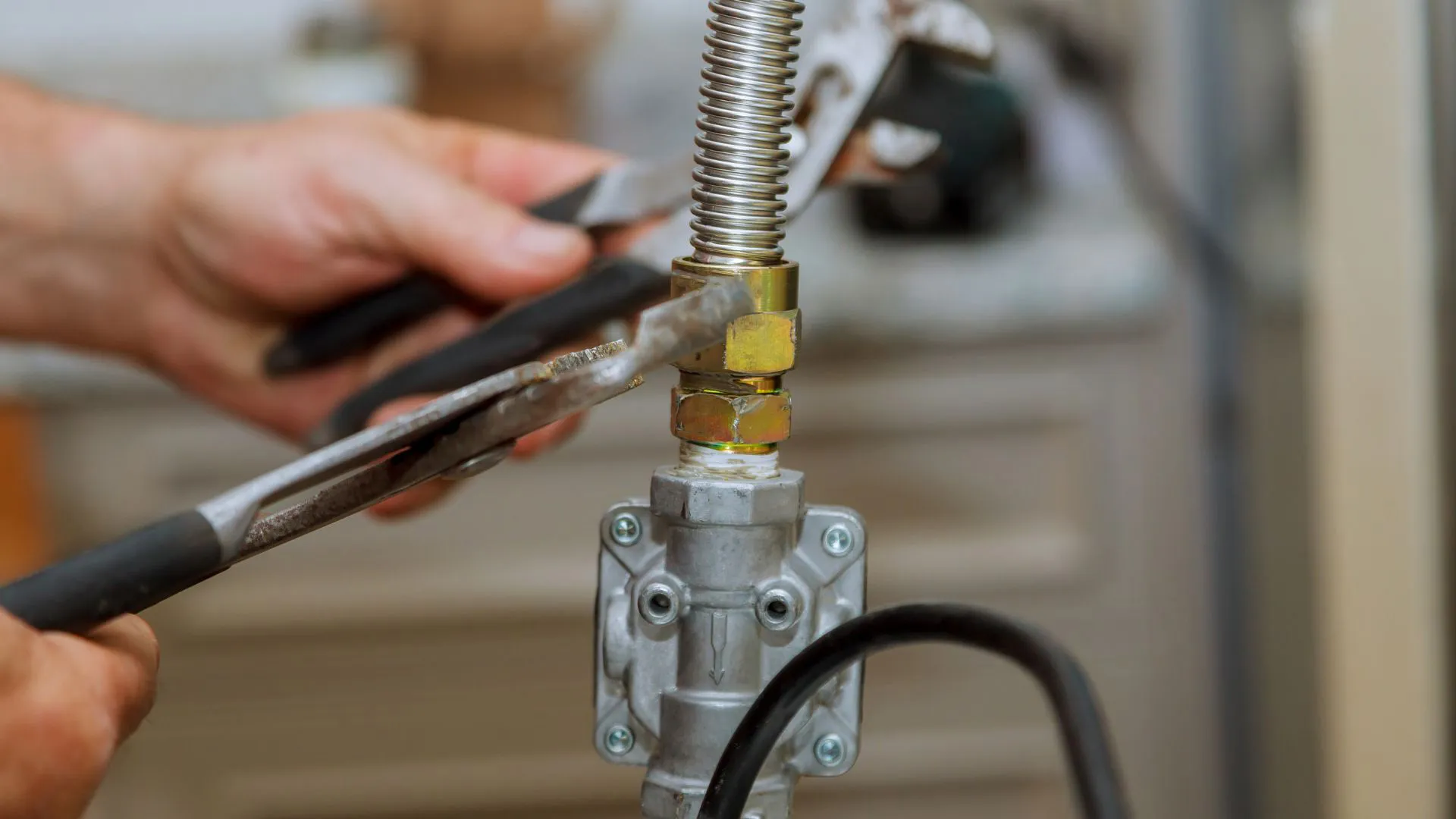 Hands using two wrenches to tighten a brass fitting on a flexible gas pipe connection.