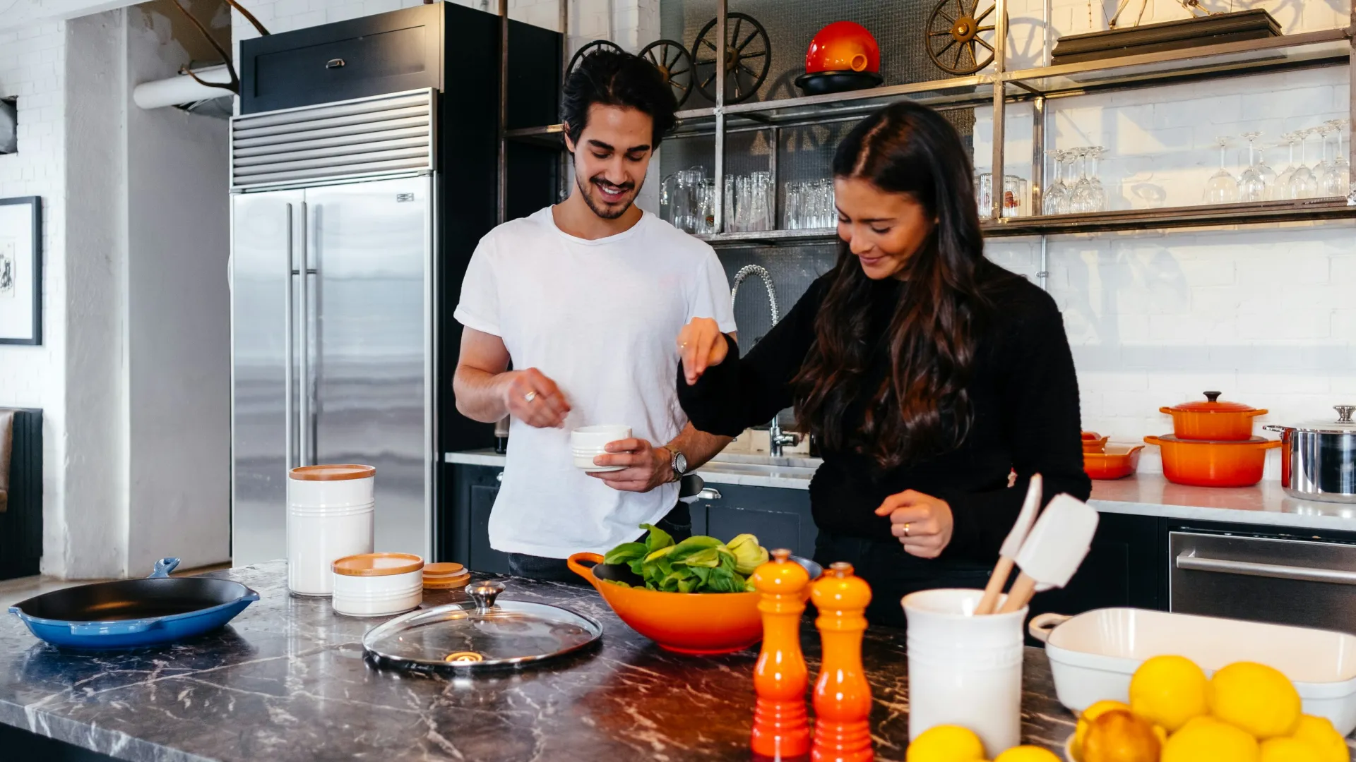 Couple cooking together in a bright kitchen with red cookware and fresh vegetables on the counter