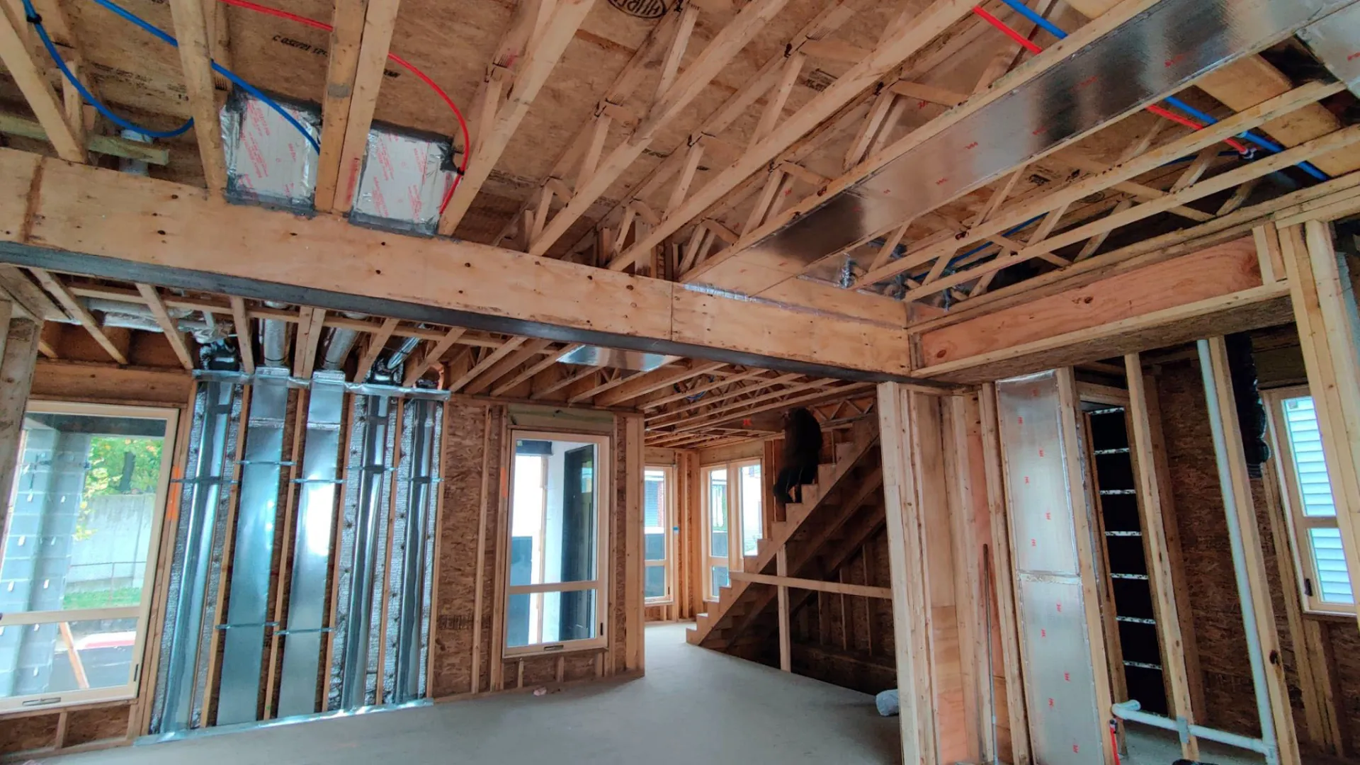 Interior view of a wooden framed house under construction with exposed beams and ductwork.