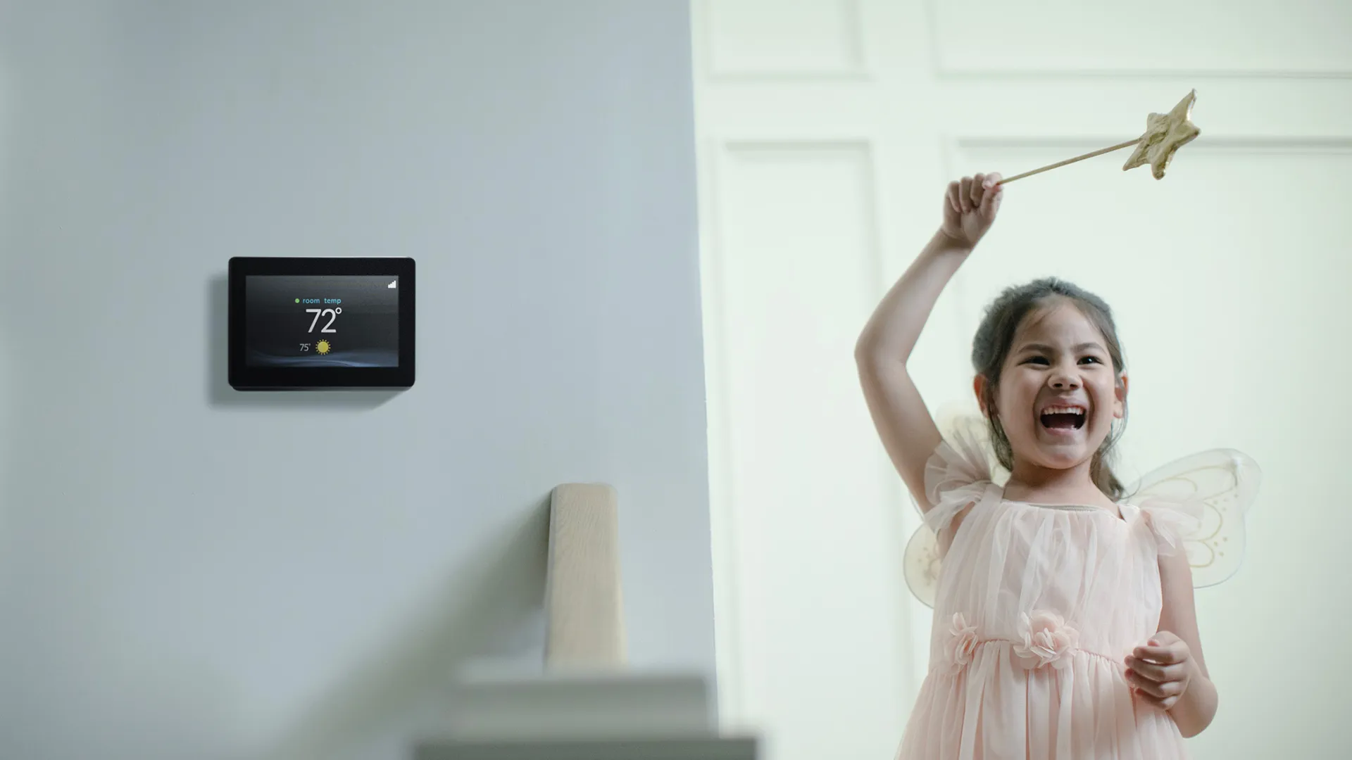 Smiling girl in fairy costume holding a star wand next to a smart thermostat displaying 72 degrees