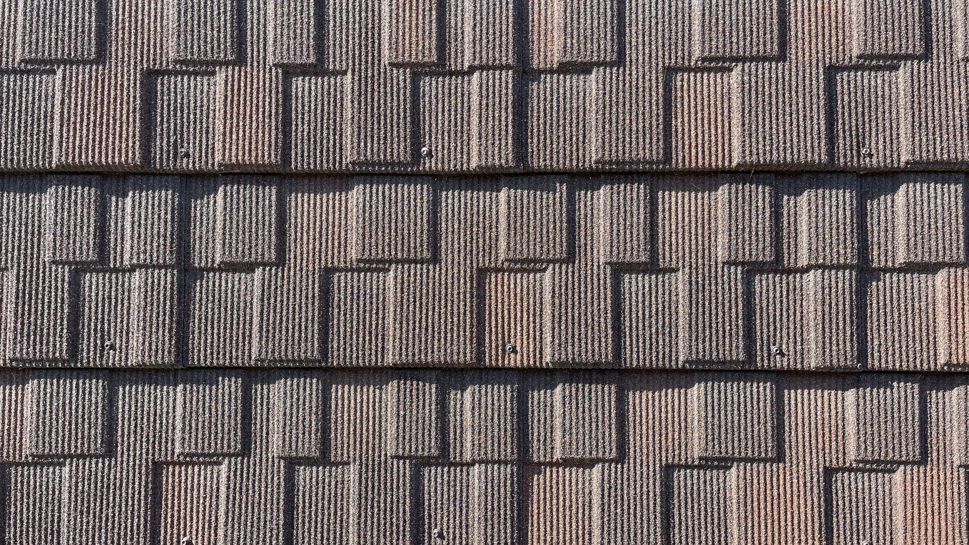 Close-up of brown textured roof shingles arranged in overlapping horizontal rows under sunlight.