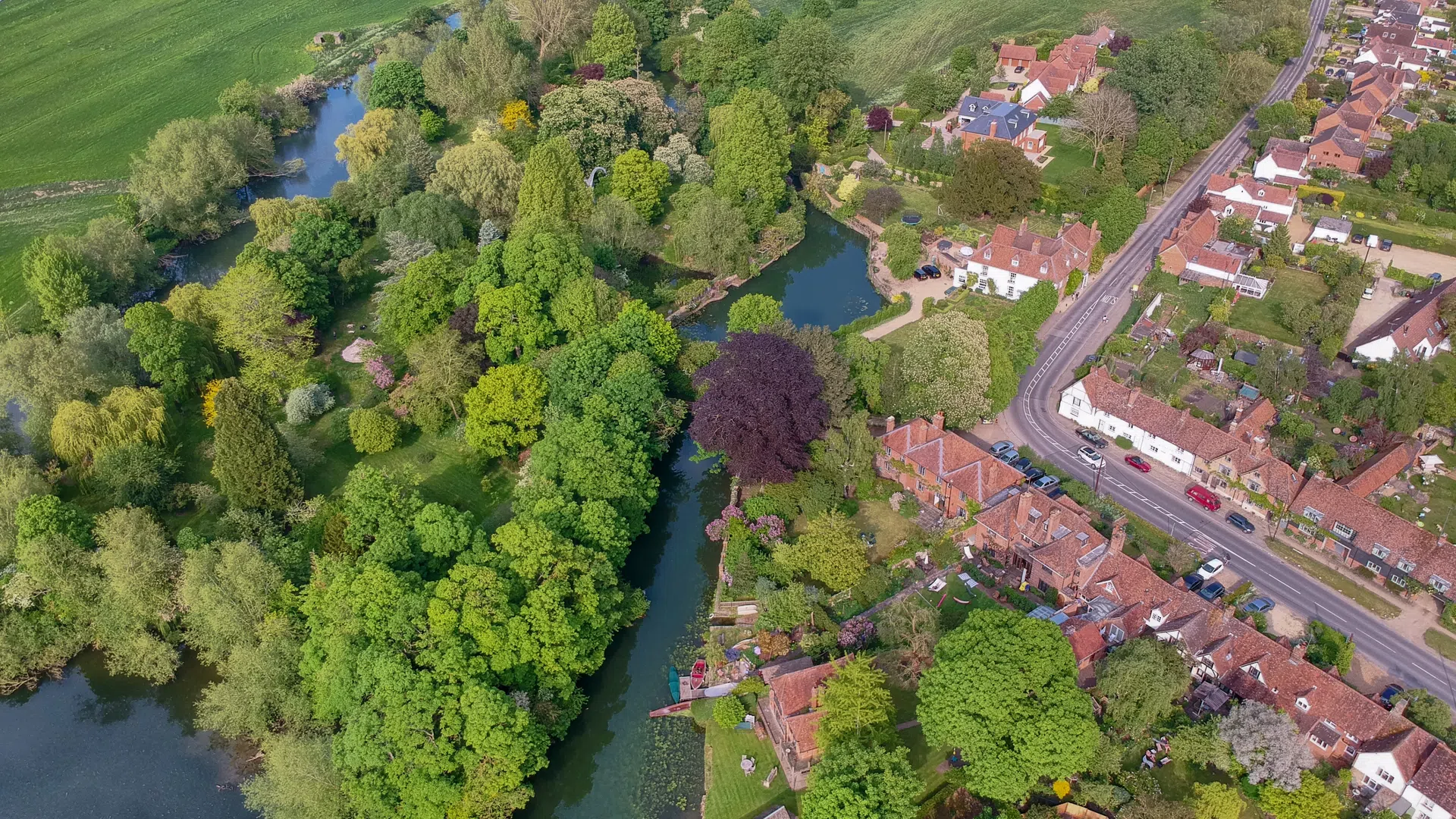 Aerial view of a river winding through lush greenery beside a residential area with houses and roads.