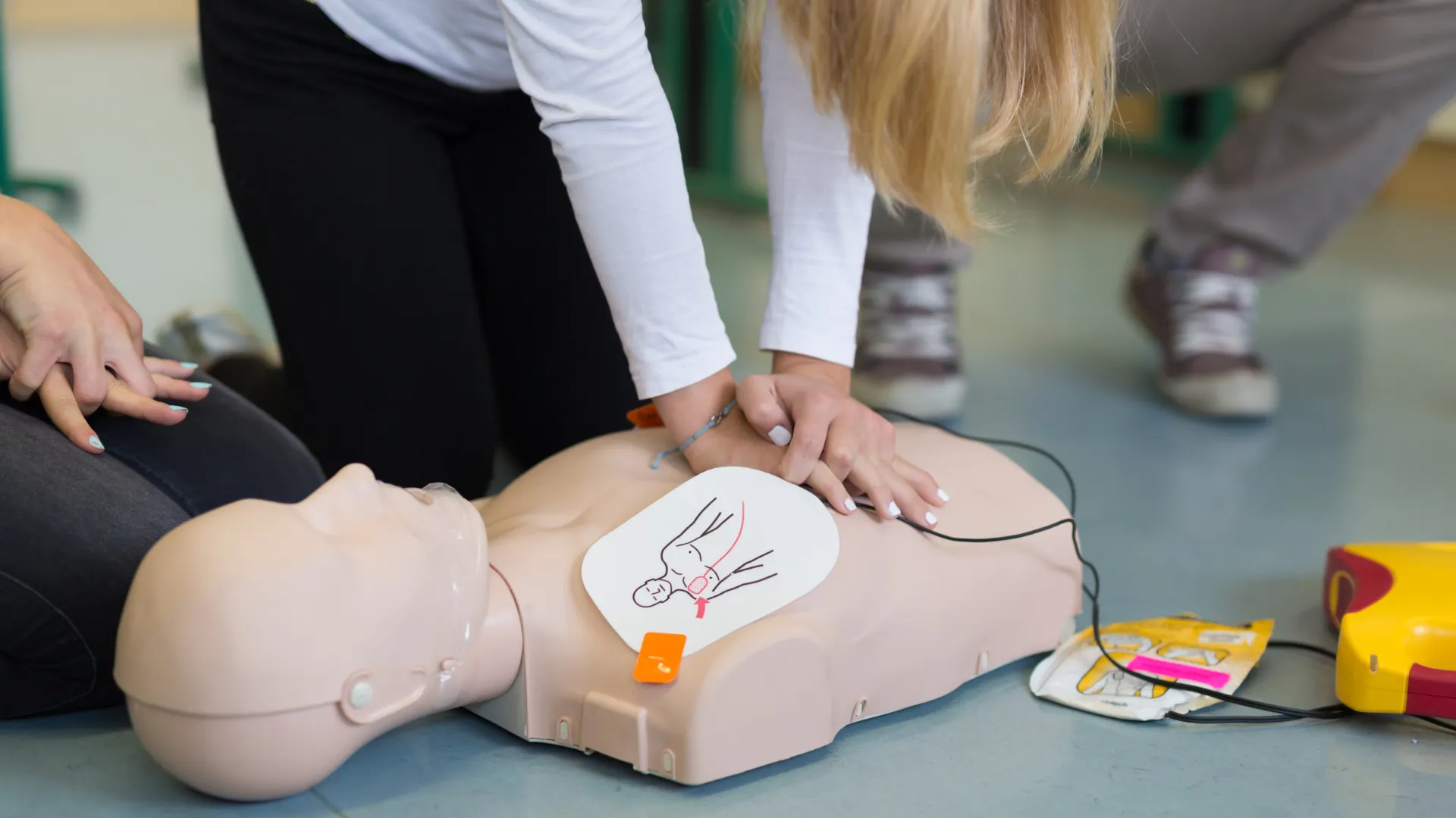 Person performing CPR on a medical training mannequin in a classroom setting.