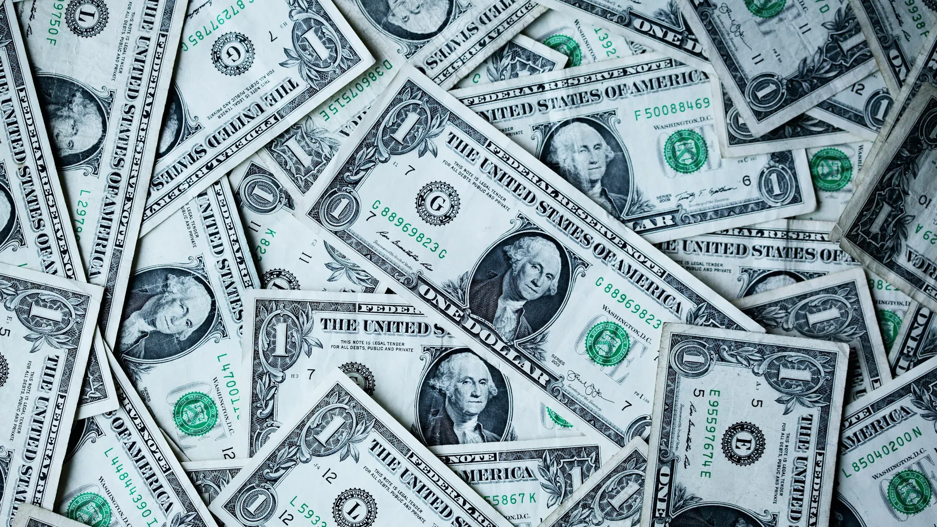 Pile of scattered one dollar US bills showing George Washington and green treasury seals.
