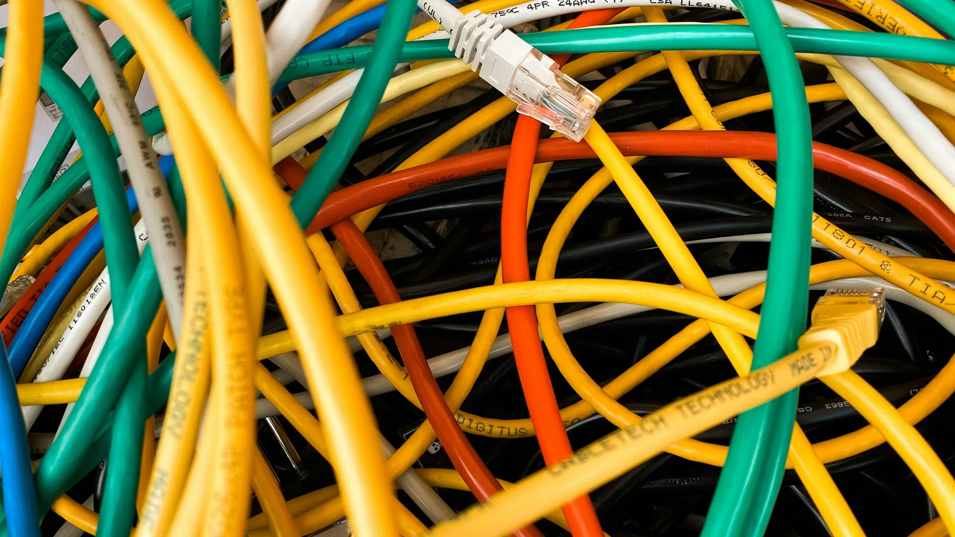 Tangled network cables in green, yellow, orange, white, and black with visible Ethernet connectors close-up.