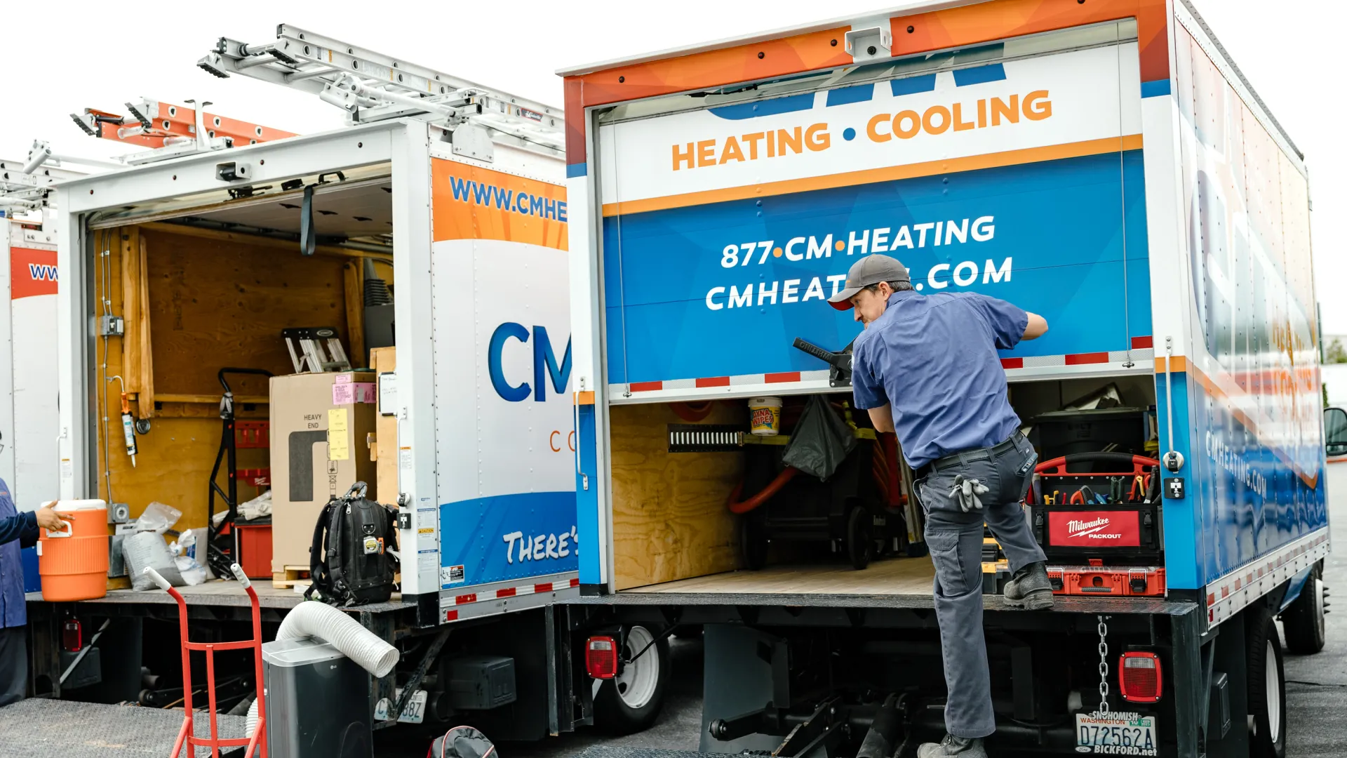 Technician unloading heating and cooling equipment from CM Heating company trucks with ladders and tools visible