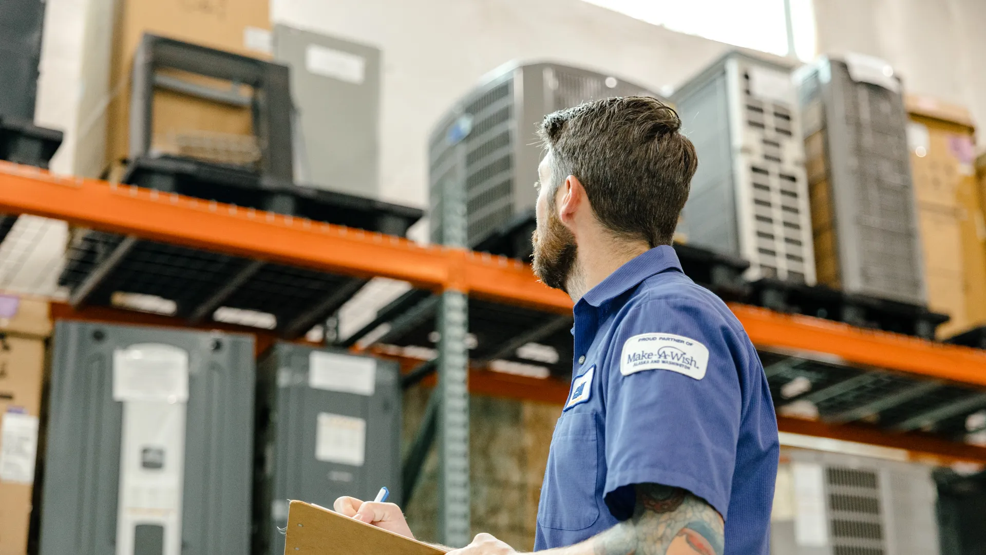 Warehouse worker with clipboard inspecting inventory on high metal shelves in storage facility.